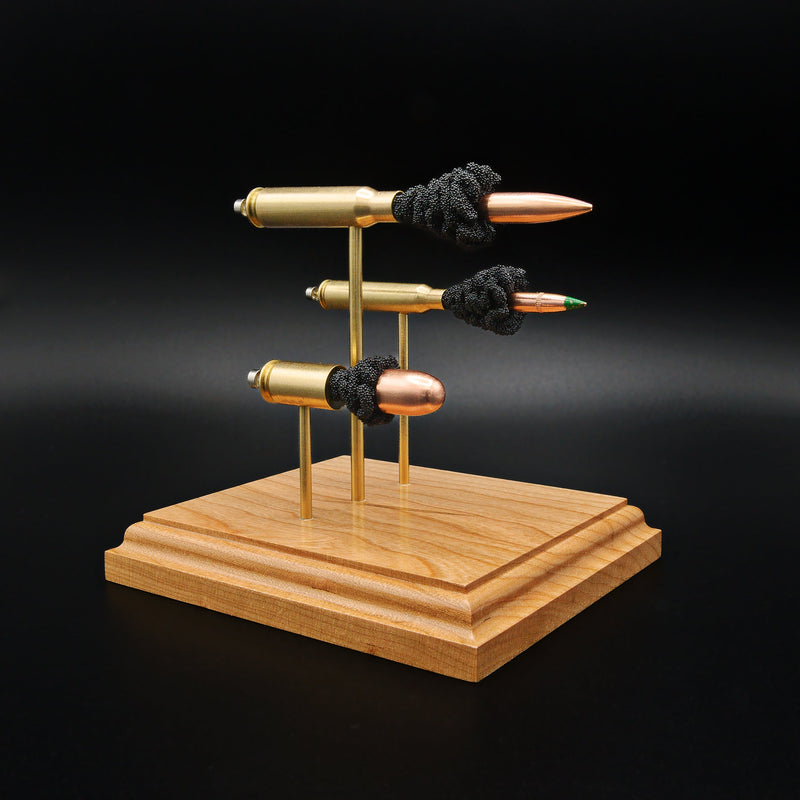 Front left angle of a triple caliber anatomy ammunition display showcasing a .308 Winchester Sierra MatchKing HPBT, 5.56×45mm M855 Green Tip, and .45 Auto Sierra FMJ with simulated powder on a handcrafted cherry wood base.