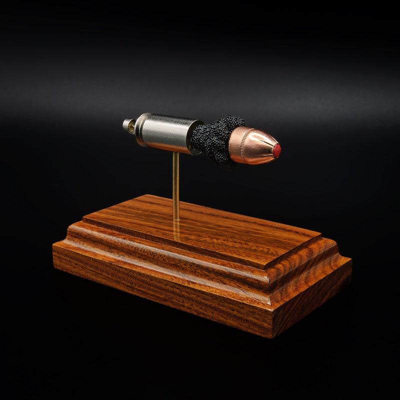 Angled view of a .45 Auto cartridge model on a rosewood base, highlighting the red polymer tip and textured powder between components