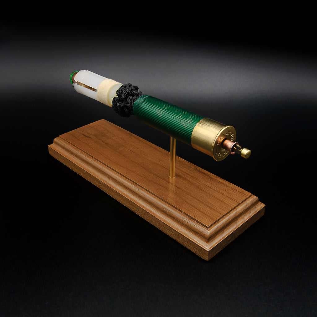 Elevated rear three-quarter view of an exploded Remington 12 Gauge AccuTip shotgun shell display showcasing the brass head, expanded primer cup, anvil, battery cup, green hull, exposed simulated powder, sabot, copper slug with green polymer tip, and handcrafted walnut presentation base.