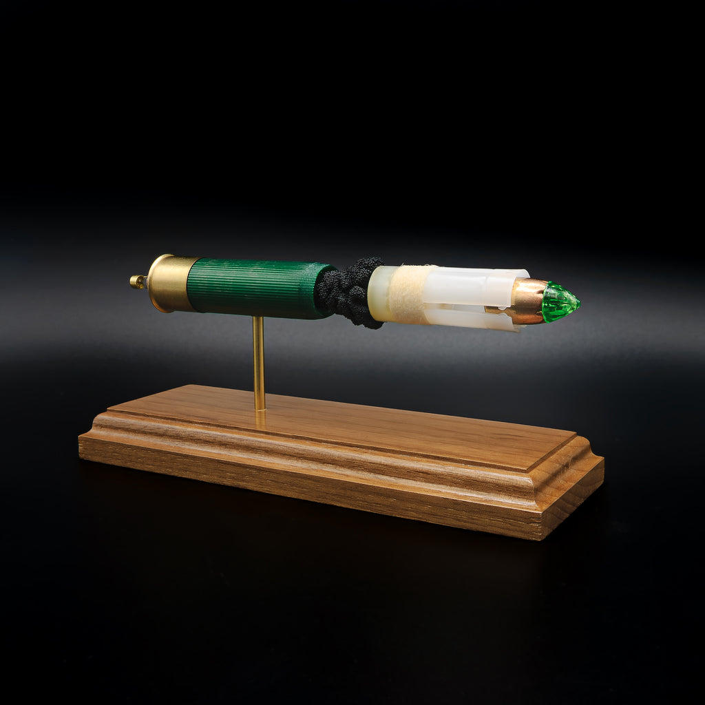 Front-right three-quarter view of a handcrafted Remington 12 Gauge AccuTip slug display showcasing the green shotgun hull, sabot, copper AccuTip projectile with green polymer tip, exposed simulated powder, expanded primer cup, anvil, battery cup, and walnut presentation base.