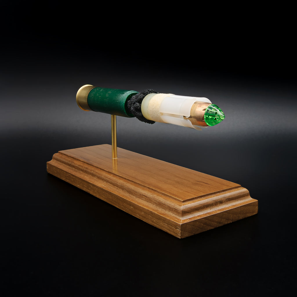 Right-front angle of an inert Remington 12 Gauge AccuTip shotgun shell display highlighting the sabot-encased slug, green polymer tip, exposed simulated powder, expanded primer assembly, and handcrafted walnut wood base.