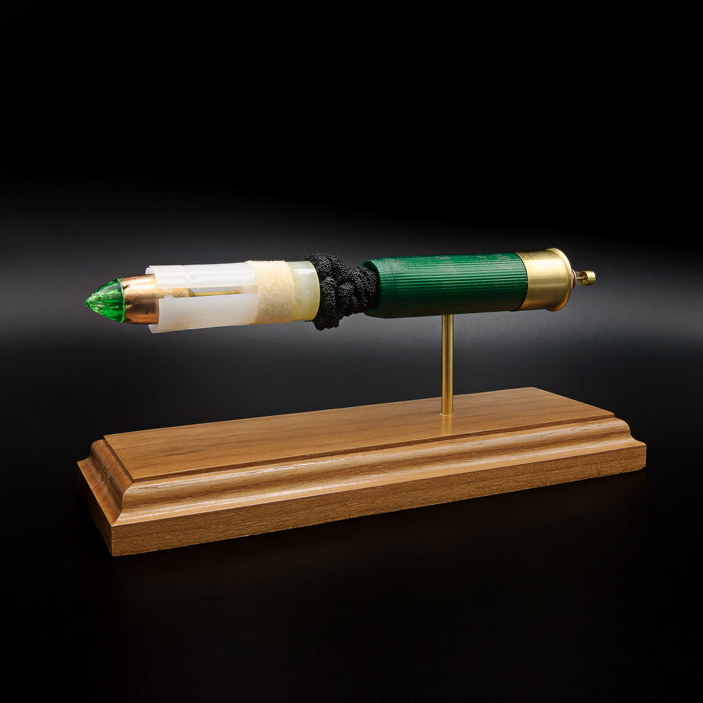 Left-side profile of an exploded Remington 12 Gauge AccuTip shotgun shell display with the green hull separated from the sabot and copper slug by exposed simulated powder while showcasing the expanded primer cup, anvil, and battery cup on a handcrafted walnut base.
