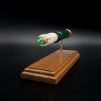 Front-left three-quarter view of an inert Remington 12 Gauge AccuTip display highlighting the sabot surrounding the copper slug with green polymer tip, exposed simulated powder, expanded primer assembly including the primer cup, anvil, and battery cup, and walnut presentation base.