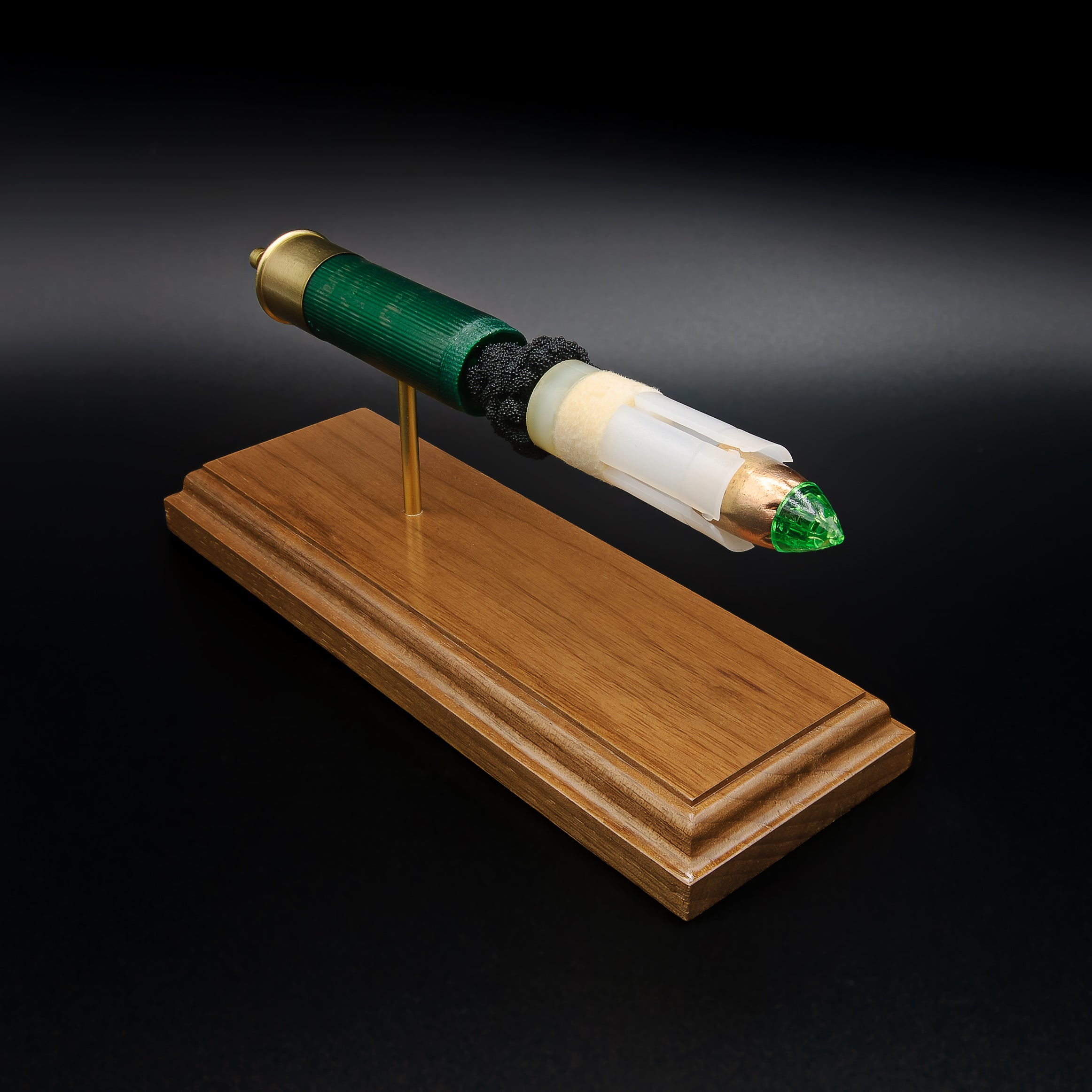 Close front perspective of a handcrafted exploded Remington 12 Gauge AccuTip slug display focusing on the green polymer tip, copper slug, sabot, exposed simulated powder, green hull, expanded primer cup, anvil, battery cup, and walnut wood base.