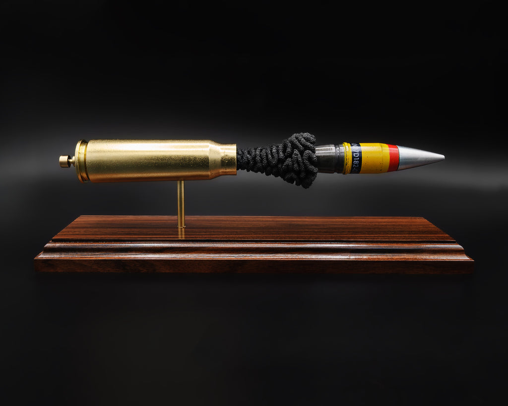 A 20mm Vulcan SAPHEI cartridge displayed in an exploded layout on a Bolivian rosewood base, with the casing and projectile separated and aligned
