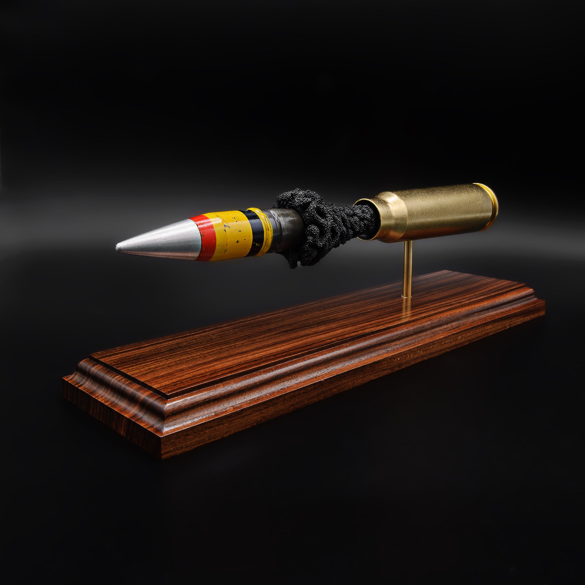 Front angled view of a 20mm Vulcan SAPHEI projectile with colored bands, positioned ahead of the casing on a rosewood base