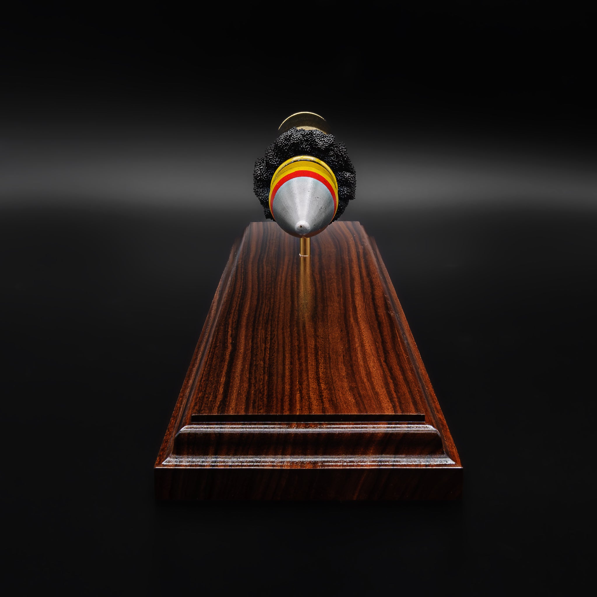 Front view of a 20mm Vulcan SAPHEI projectile centered over a Bolivian rosewood base, showing the pointed tip and symmetrical alignment