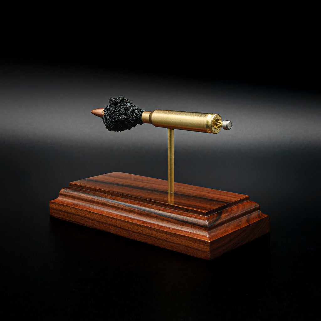 Detailed perspective of a .223 Remington FMJ exploded cartridge display mounted on a handcrafted Bolivian rosewood base, revealing the bullet, brass case, simulated powder, and expanded primer assembly including the primer cup, anvil, and battery cup.