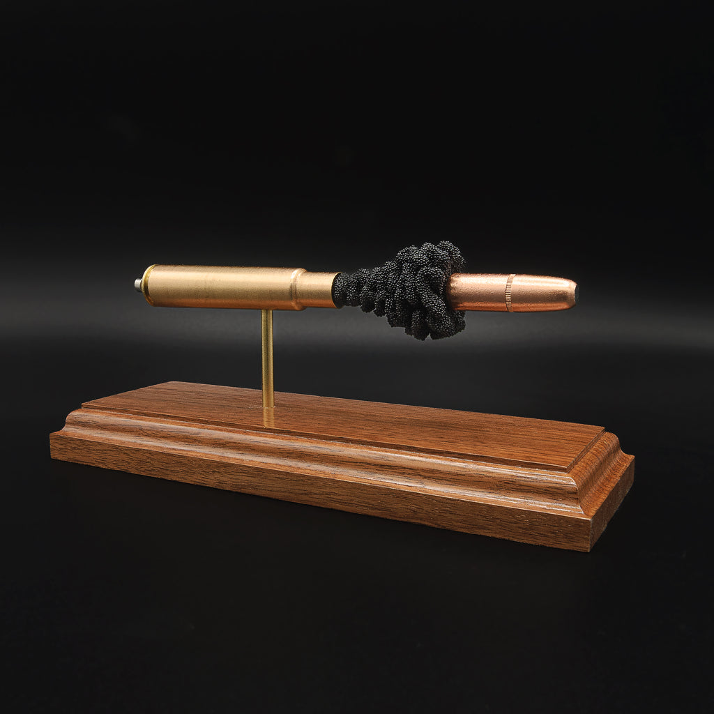 Angled view of a .416 Rigby Hornady DGX cartridge anatomy display highlighting the projectile, simulated powder, cartridge case, primer cup, and anvil on a walnut wood base.