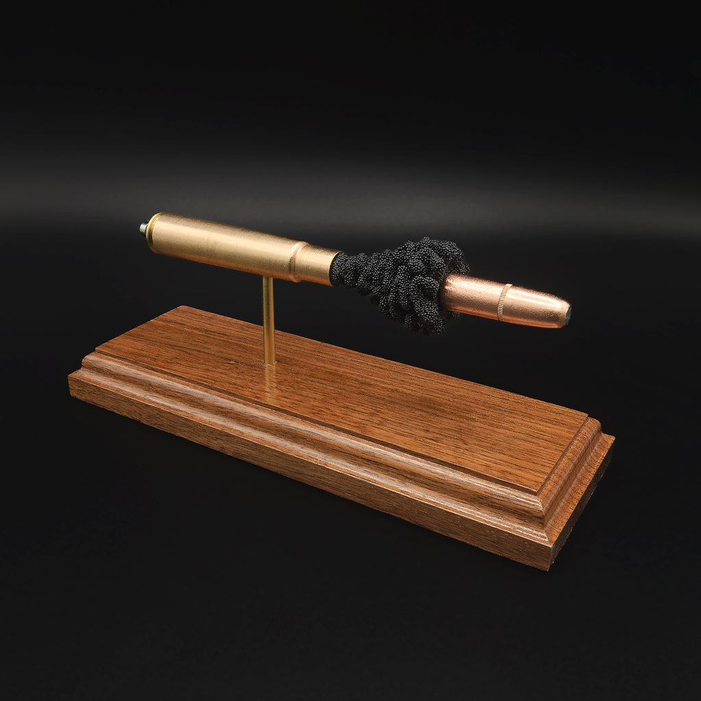 Close angled view of a .416 Rigby Hornady DGX cartridge anatomy display highlighting the DGX projectile, simulated powder, cartridge case, primer cup, and anvil on a walnut wood base.