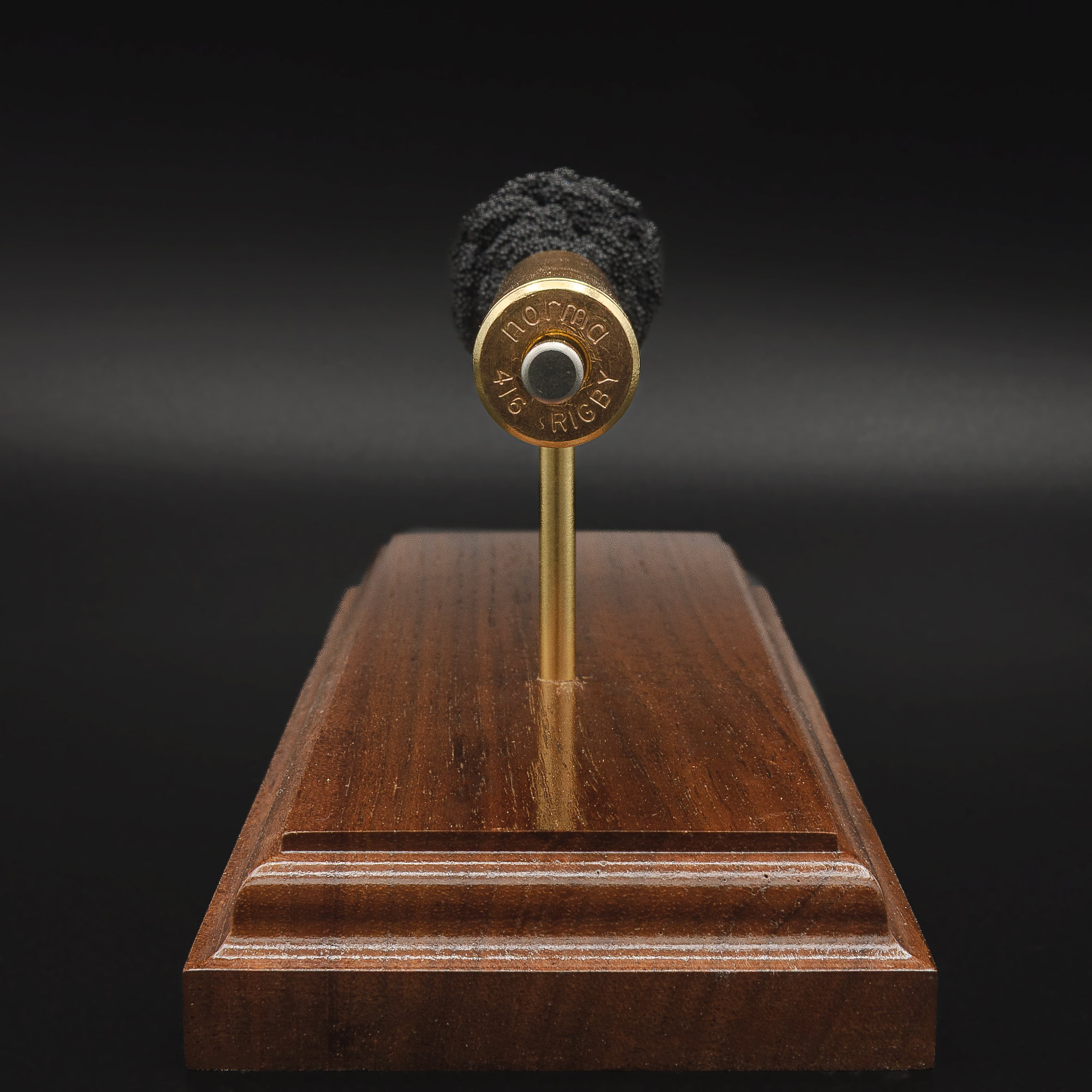 Rear view of a .416 Rigby Hornady DGX cartridge anatomy display showing the cartridge case head, primer cup, anvil, simulated powder, and projectile on a walnut wood base.
