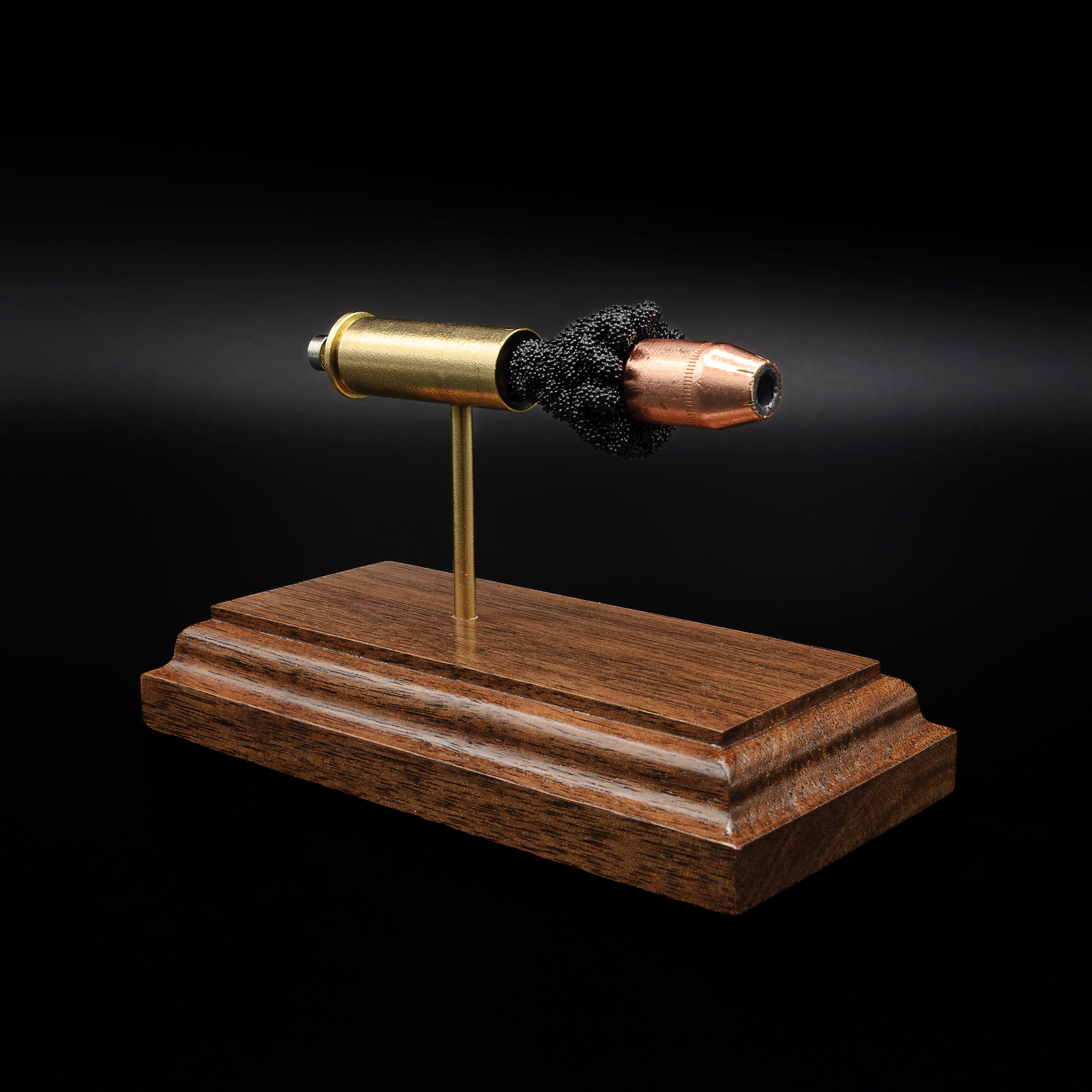 Angled view of a .44 Magnum cartridge model on a walnut base, showing the hollow point bullet and textured black powder between the components