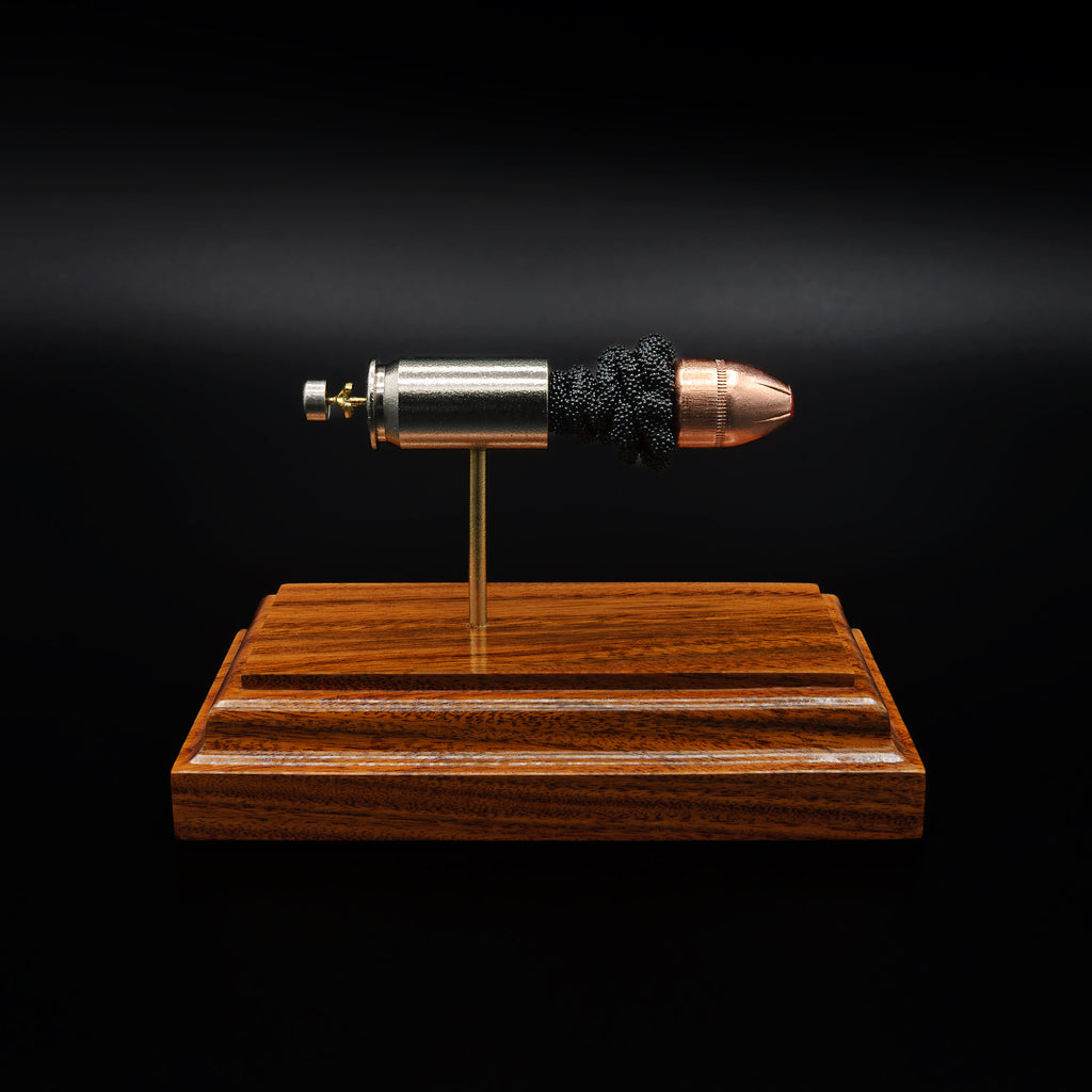 A .45 Auto cartridge displayed in an exploded layout on a rosewood base, with the nickel case, powder cluster, and polymer-tipped bullet aligned in a straight line