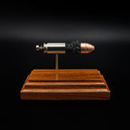 A .45 Auto cartridge displayed in an exploded layout on a rosewood base, with the nickel case, powder cluster, and polymer-tipped bullet aligned in a straight line