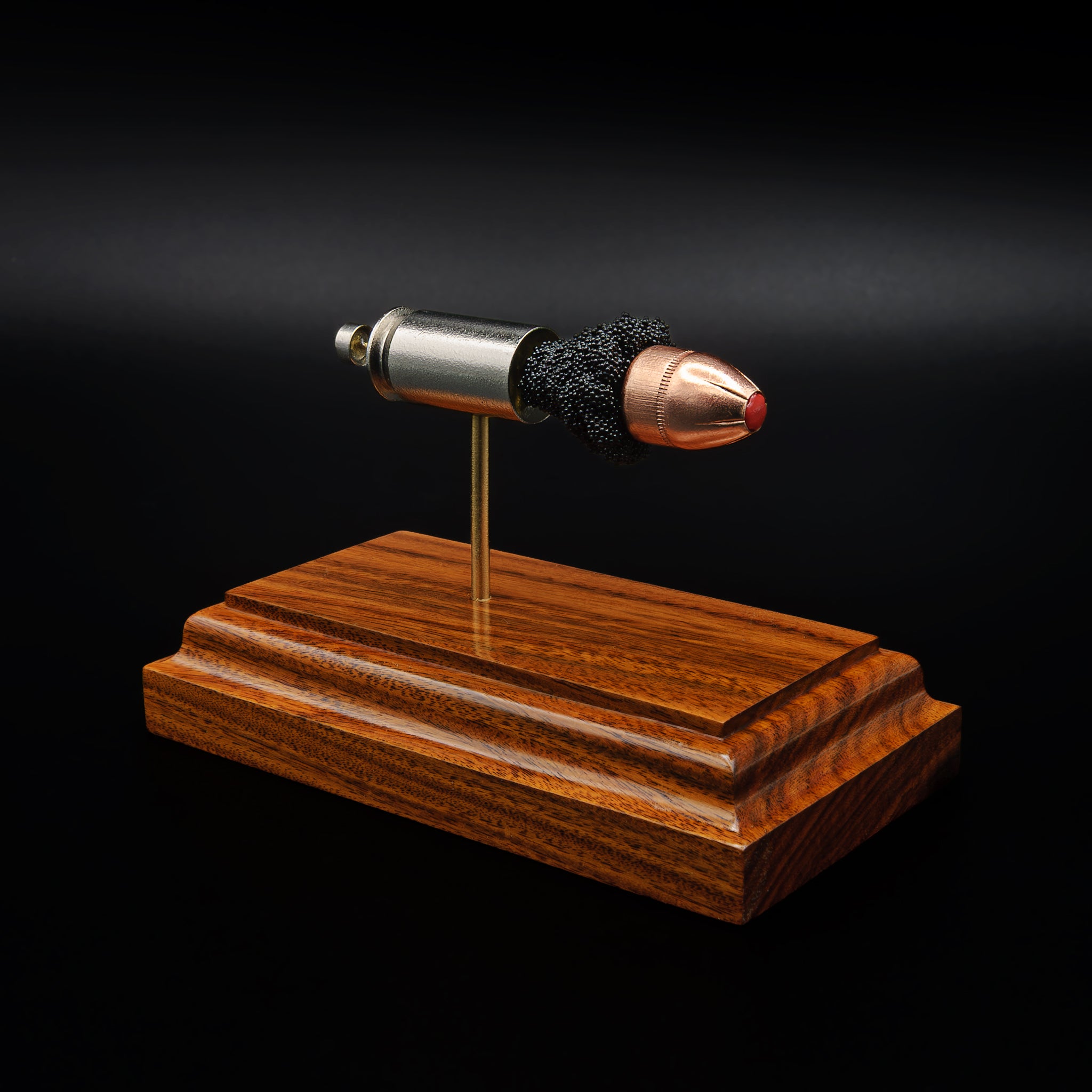 Angled view of a .45 Auto cartridge model on a rosewood base, highlighting the red polymer tip and textured powder between components