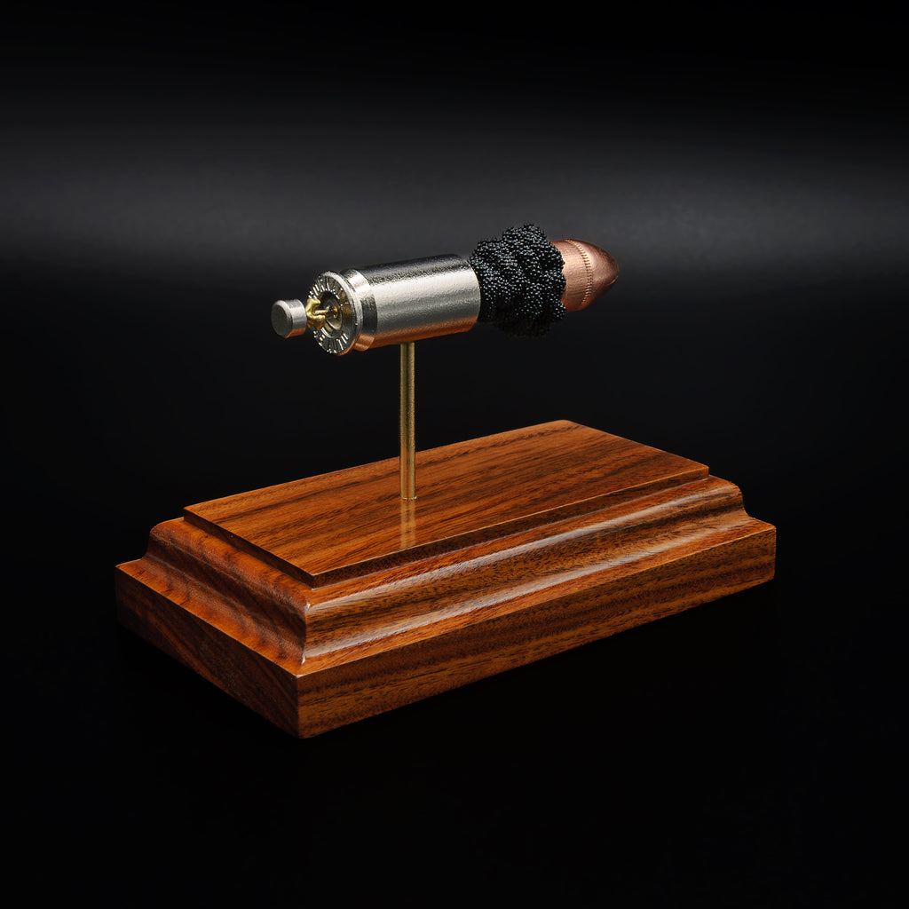 Rear view of a .45 Auto cartridge display showing the base of the nickel casing and primer mounted above a rosewood base