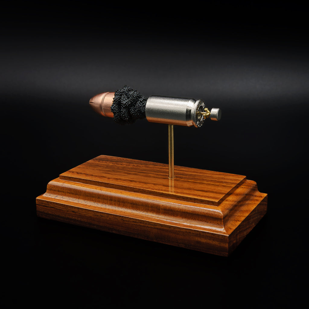 Side view of a .45 Auto cartridge model facing the opposite direction, showing the alignment of the bullet, powder, and casing on a wood base