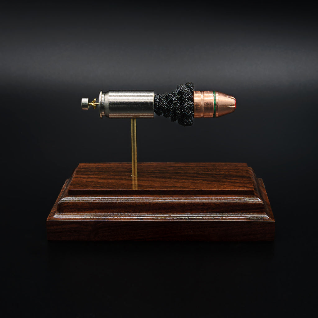 A .45 Auto cartridge displayed in an exploded layout on a rosewood base, featuring a nickel case, powder cluster, and Hornady Critical Duty bullet with FlexLock tip aligned in a straight line