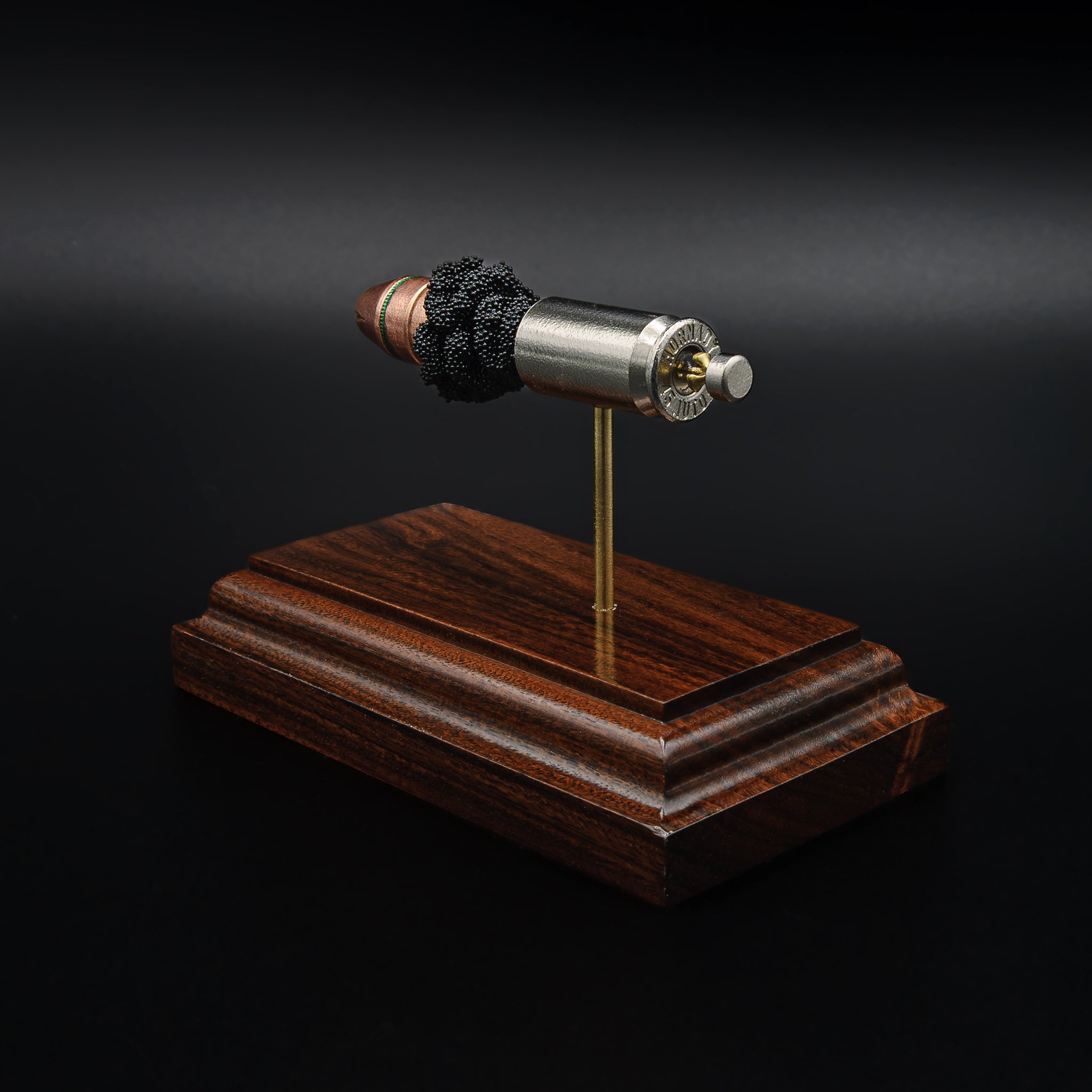 Rear view of a .45 Auto cartridge display showing the base of the nickel casing and primer mounted above a rosewood base