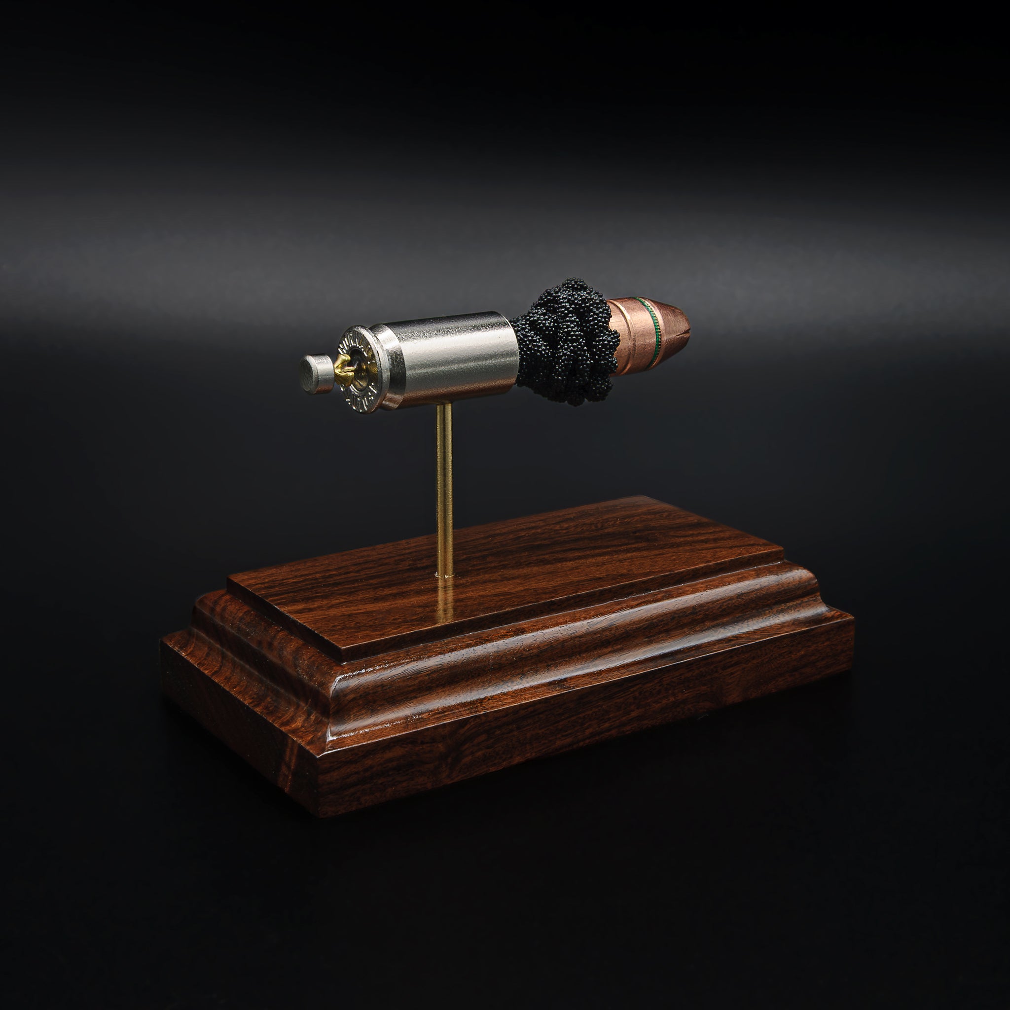 Rear view of a .45 Auto cartridge display showing the base of the nickel casing and primer mounted above a rosewood base