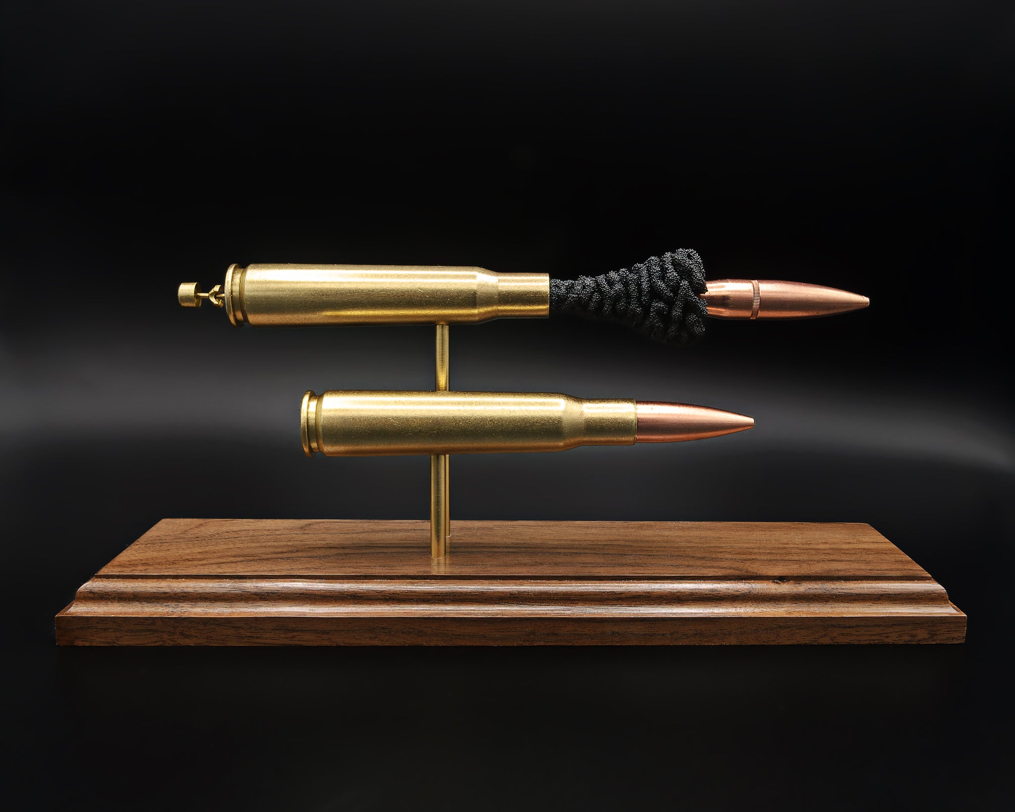 Side profile of .50 BMG comparison display featuring intact cartridge and separated components on walnut base