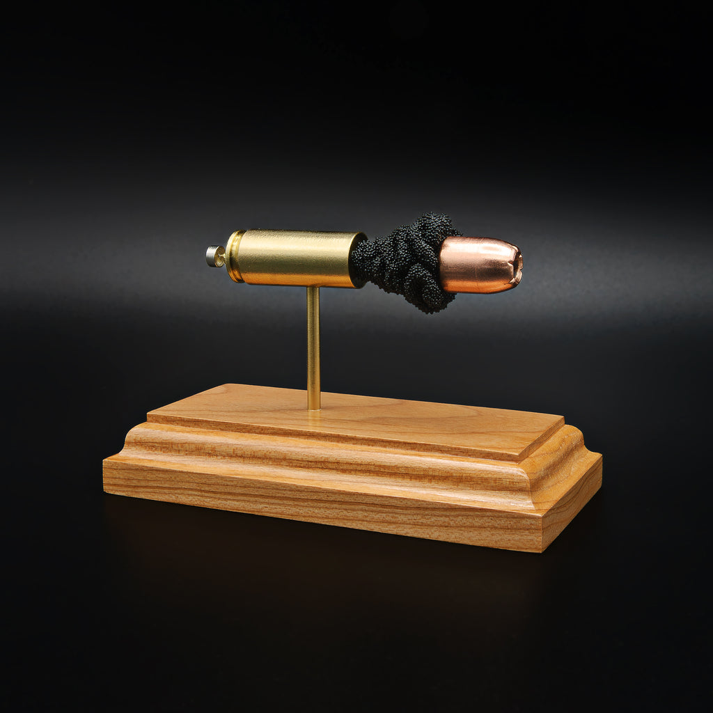 Angled view of a .50 Action Express Hornady Custom 300gr XTP cartridge anatomy display highlighting the projectile, simulated powder, cartridge case, primer cup, and anvil on a cherry wood base.