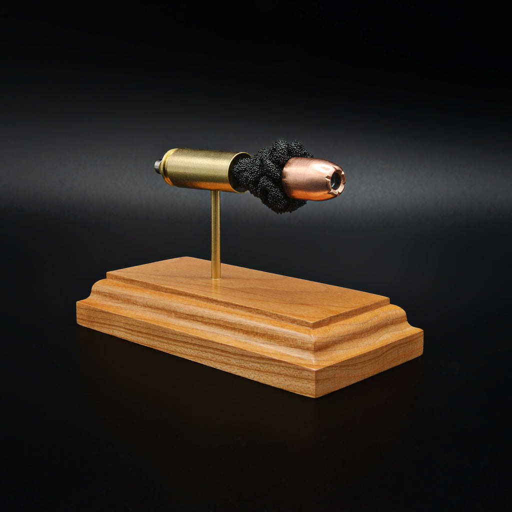 Side view of a .50 Action Express Hornady Custom 300gr XTP cartridge anatomy display with the primer cup, anvil, cartridge case, simulated powder, and projectile visible on a cherry wood base.