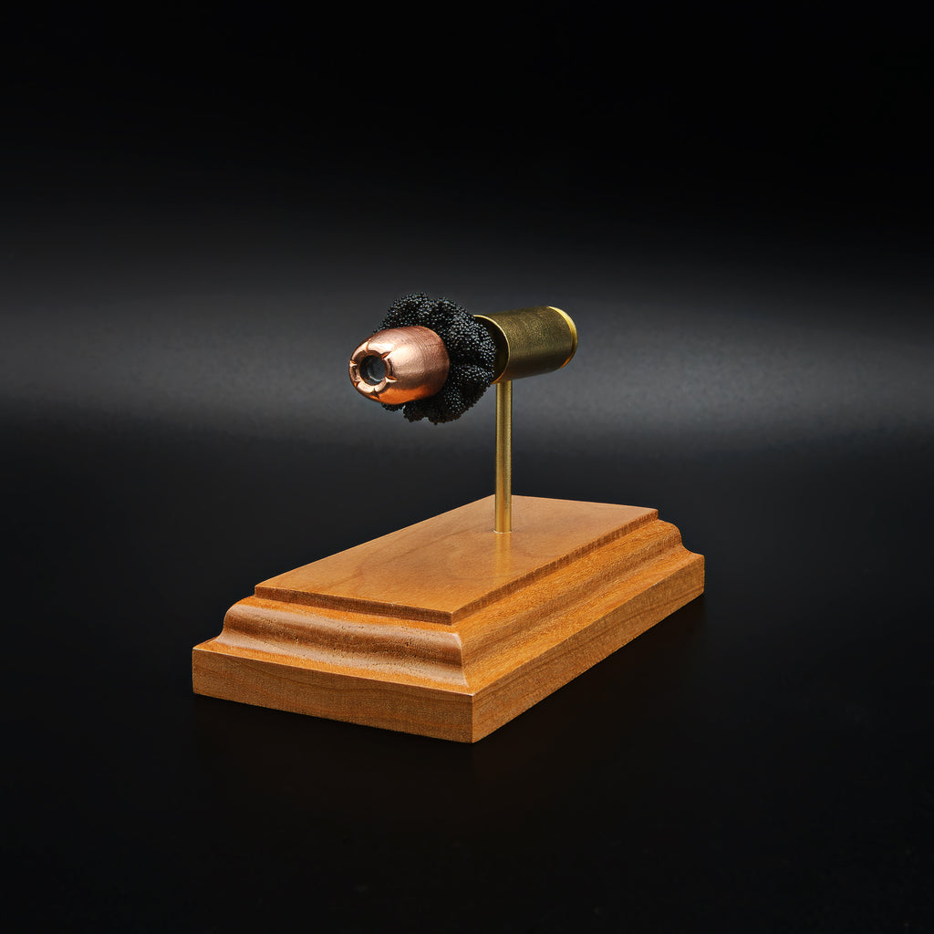 Front angled view of a .50 Action Express Hornady Custom 300gr XTP cartridge anatomy display with the primer cup, anvil, cartridge case, simulated powder, and projectile mounted on a cherry wood base.