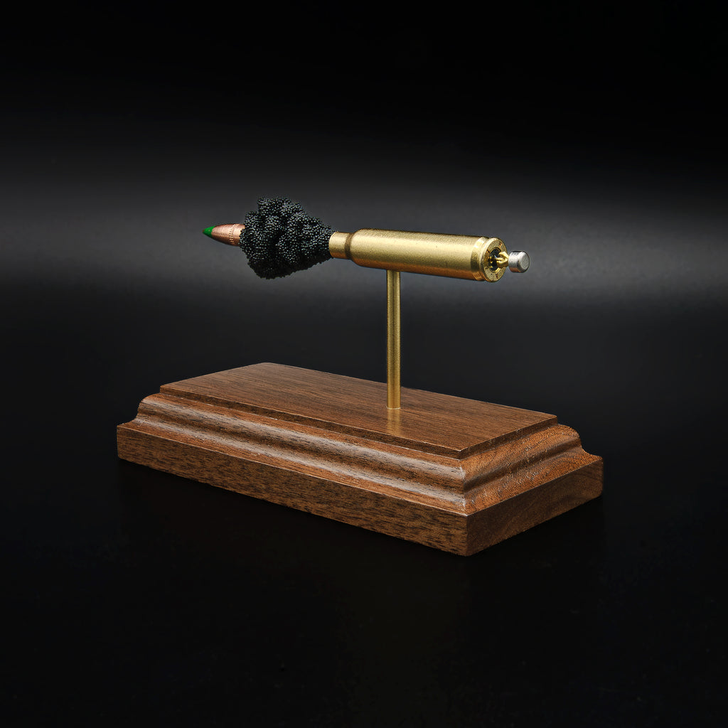 Rear view of a 5.56×45mm NATO M855 Green Tip cartridge anatomy display featuring the brass case head, primer cup, anvil, simulated powder, and projectile on a walnut base.