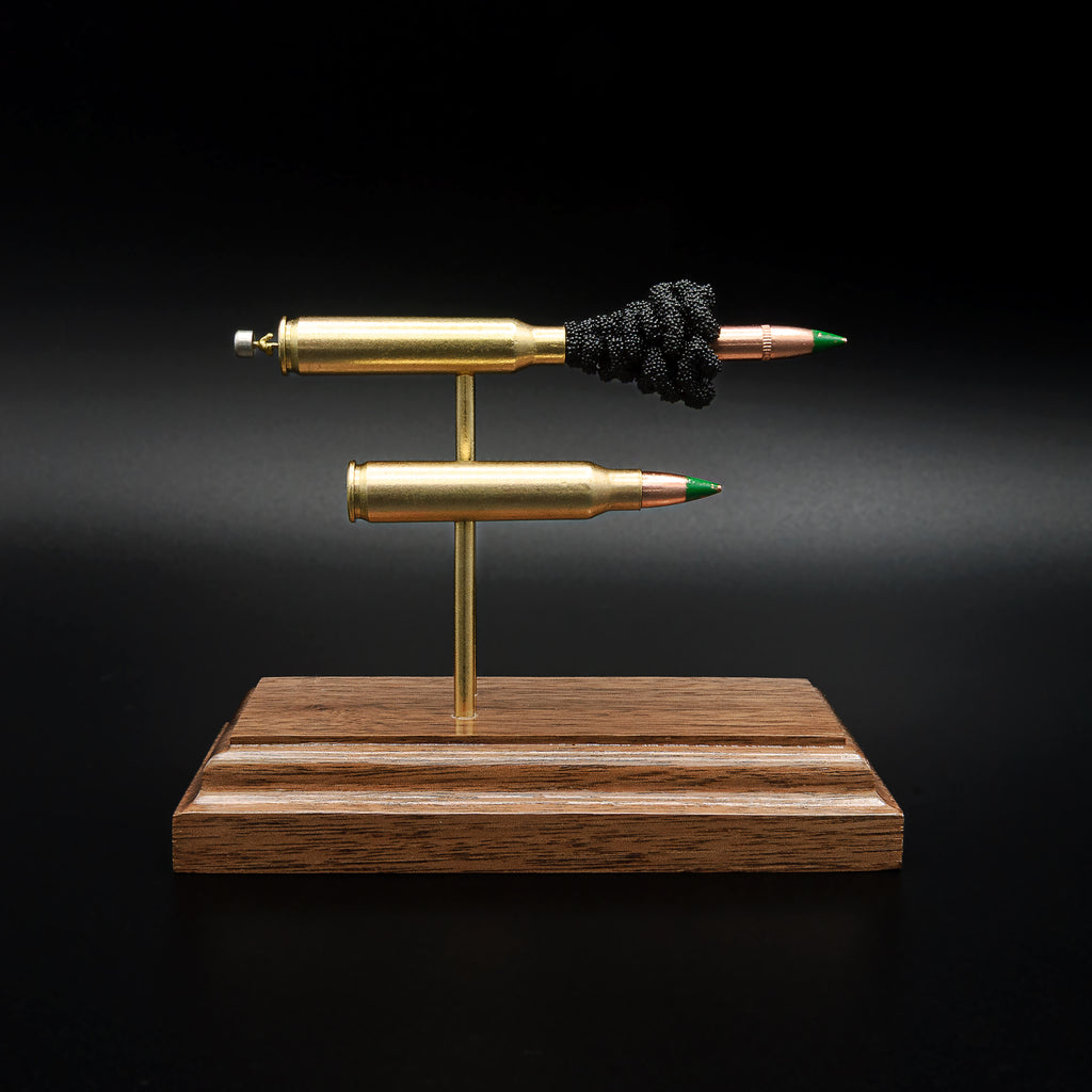 Front view of a 5.56x45 NATO SS109 Green Tip Comparison Series display featuring an exploded cartridge with exposed simulated powder displayed above a complete live cartridge on a handcrafted walnut wood base.