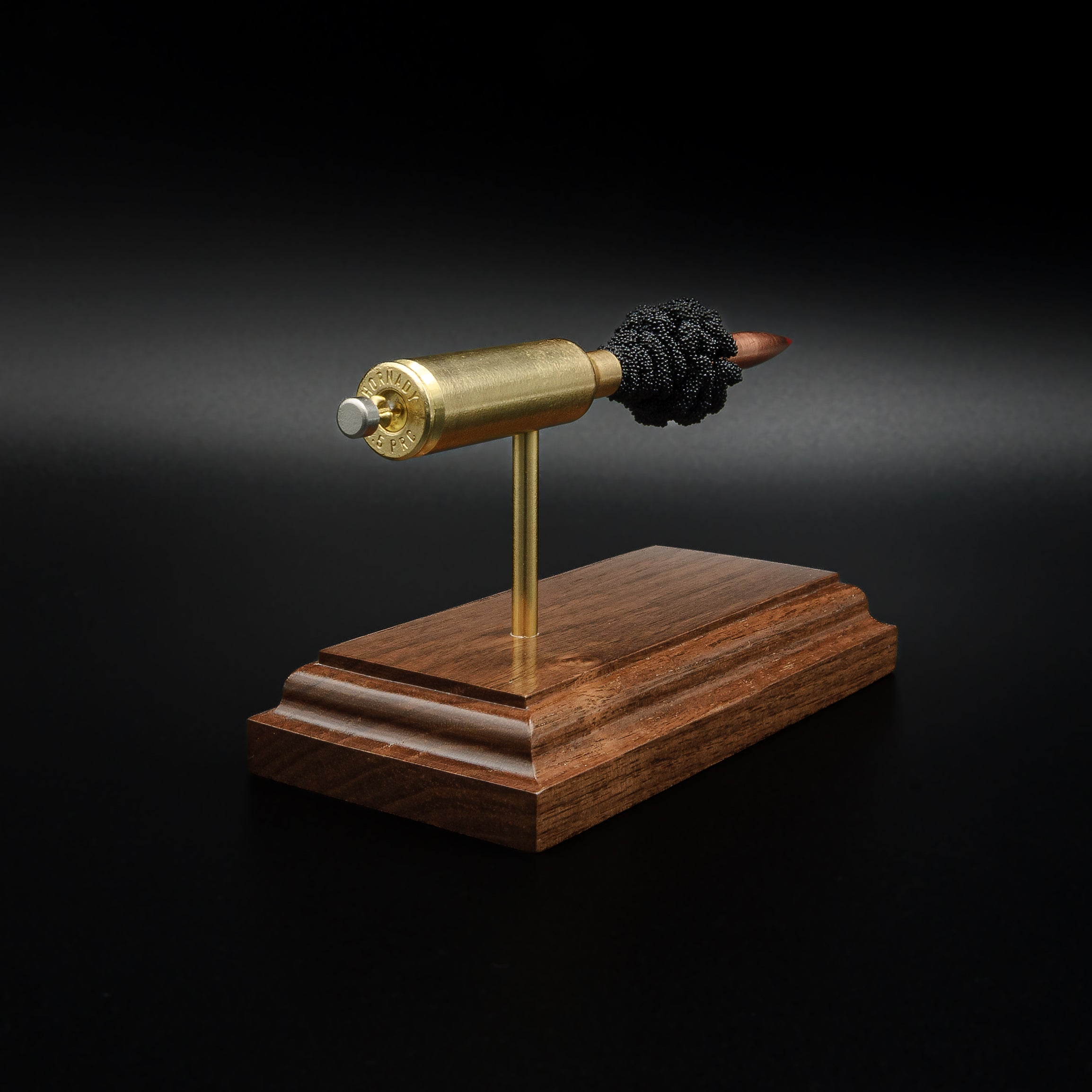 Close rear perspective of a 6.5 PRC exploded cartridge display showing the case head, primer assembly, brass case, and handcrafted walnut presentation base.