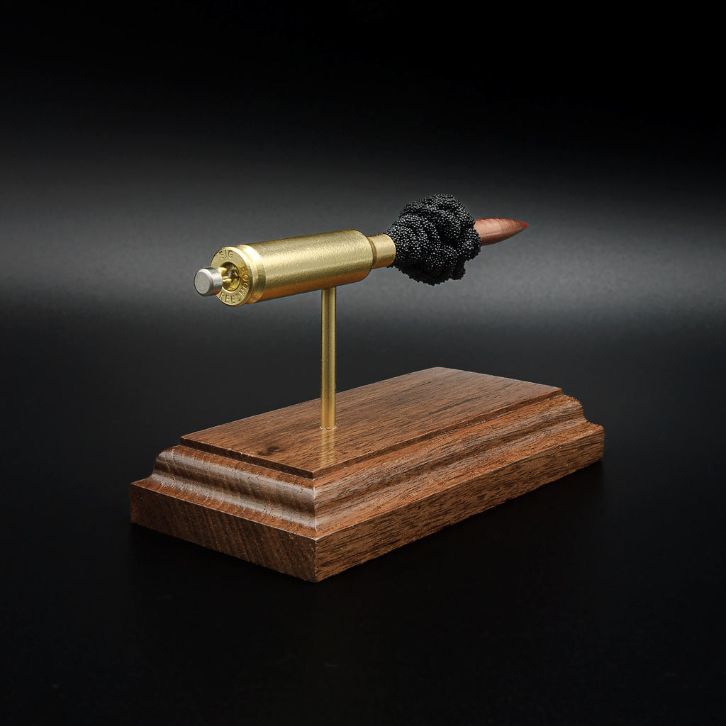 Rear three-quarter view of a 6.5 Creedmoor exploded cartridge display emphasizing the brass case head, primer assembly, and walnut presentation stand.