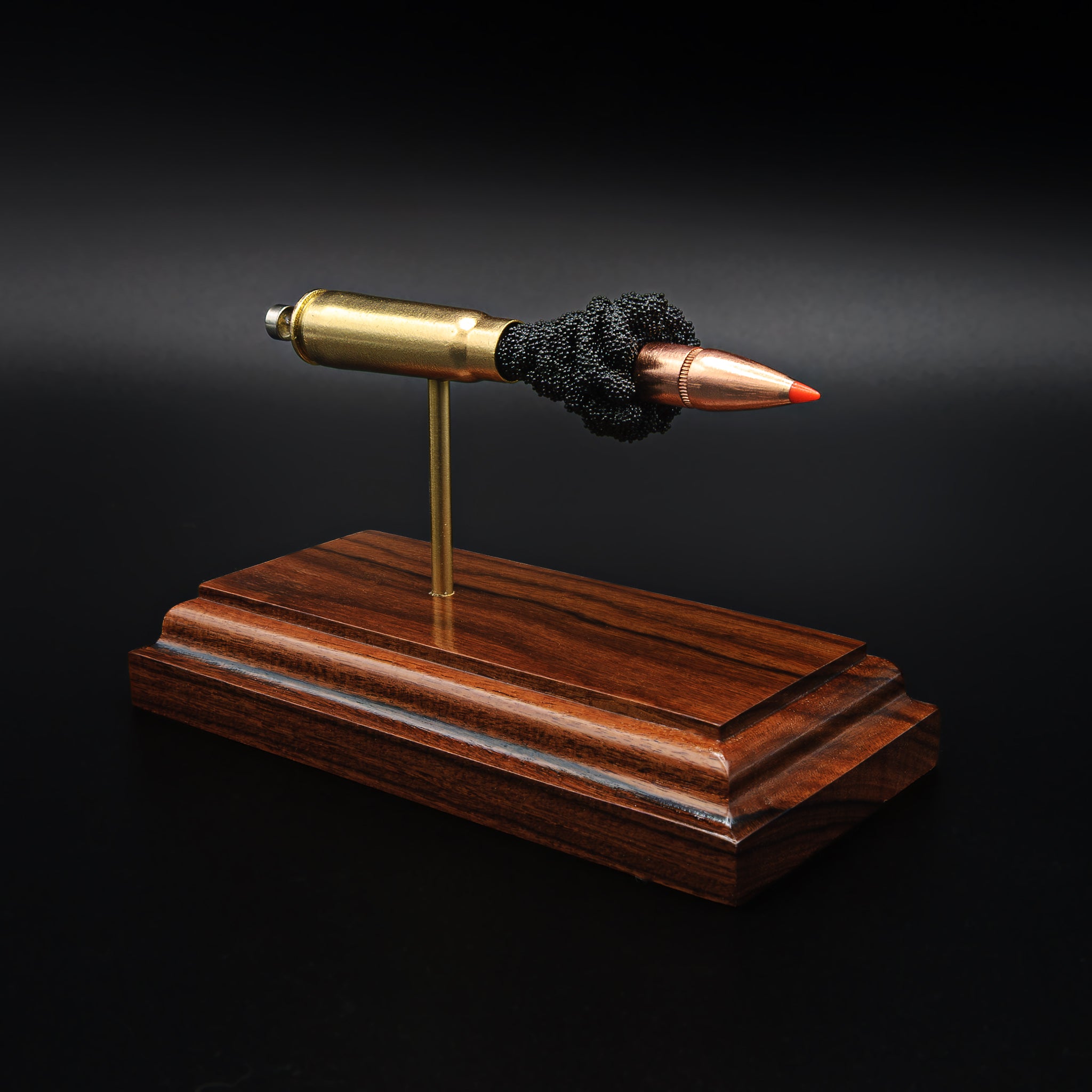 A 7.62x39 cartridge displayed in an exploded layout on a rosewood base, with the bullet, case, and internal components aligned in a straight line