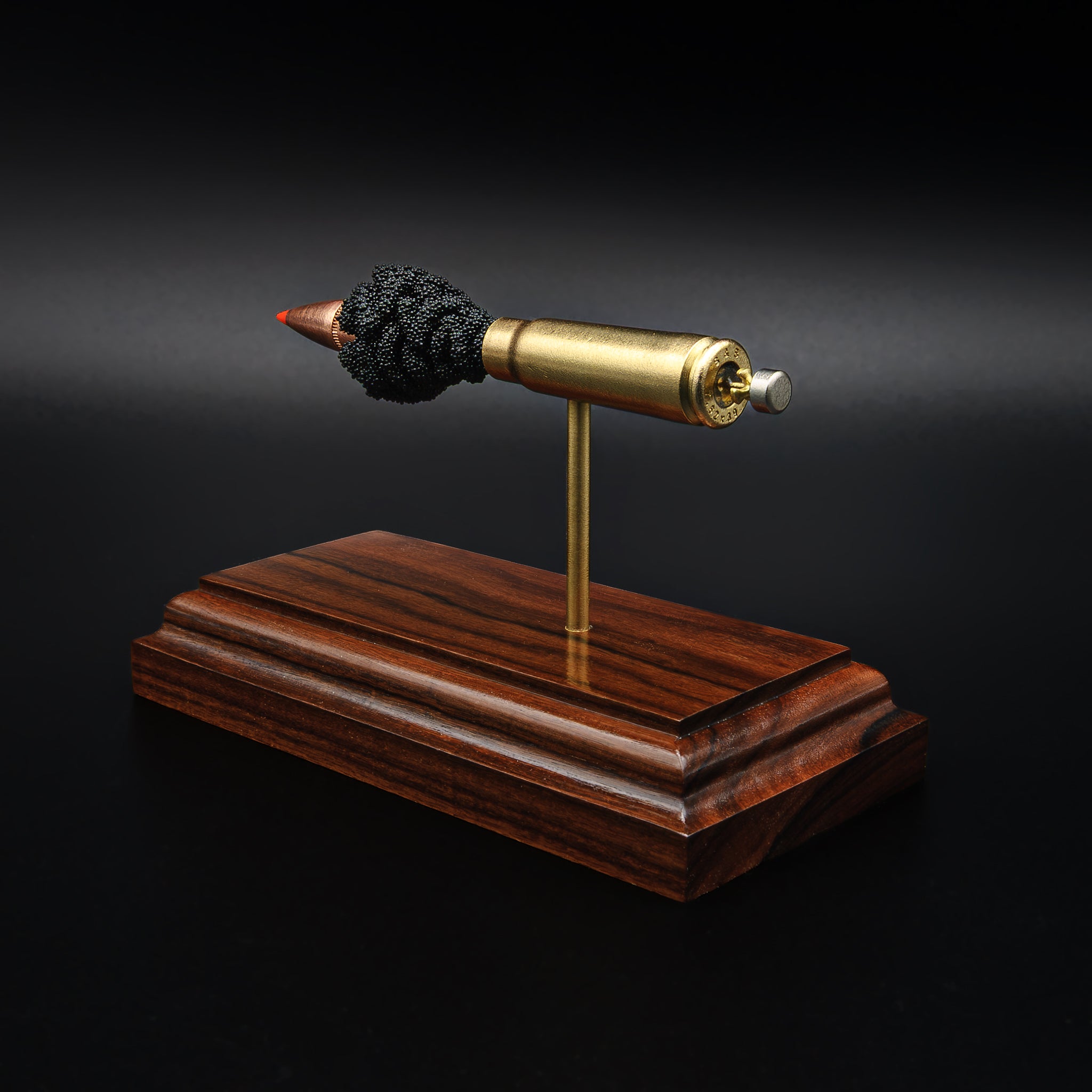 Rear angle of a 7.62x39 cartridge display showing the base of the casing and primer area, mounted on a polished rosewood platform