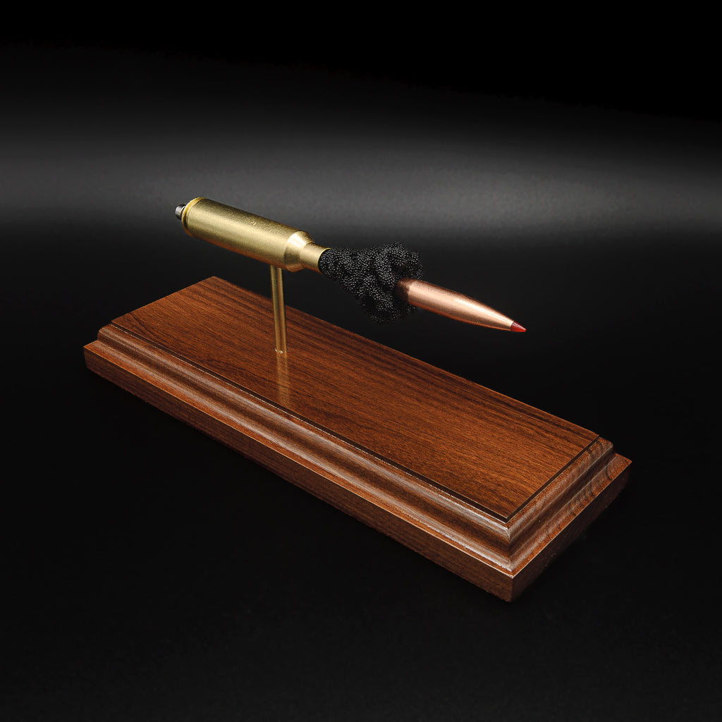 High angle front three-quarter view of a 7mm PRC Hornady 180gr ELD-M expanded cartridge display on a Bolivian Rosewood base with visible primer cup, anvil, cartridge case, simulated powder, and projectile.