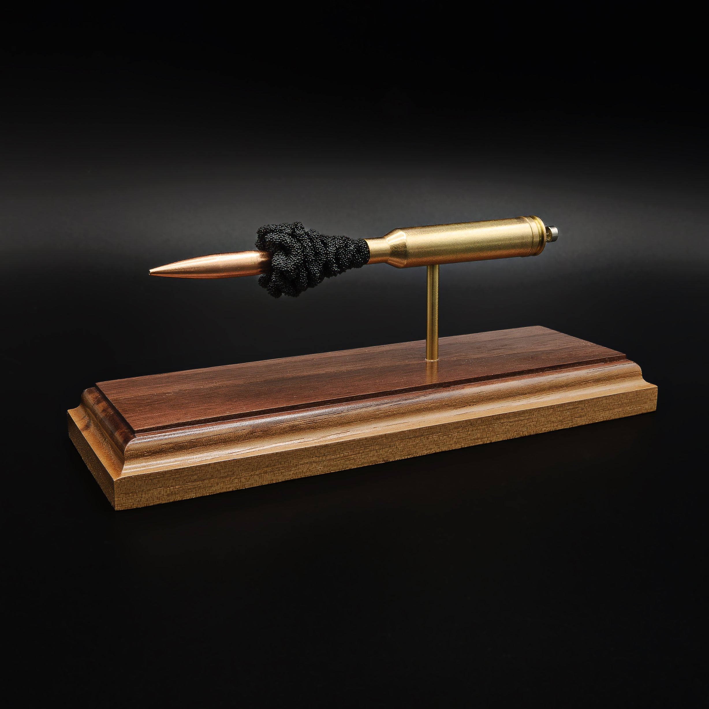 Left side profile of a 7mm Remington Magnum display with a 168 grain Berger VLD bullet separated from the case by exposed simulated powder and mounted on a handcrafted walnut base.