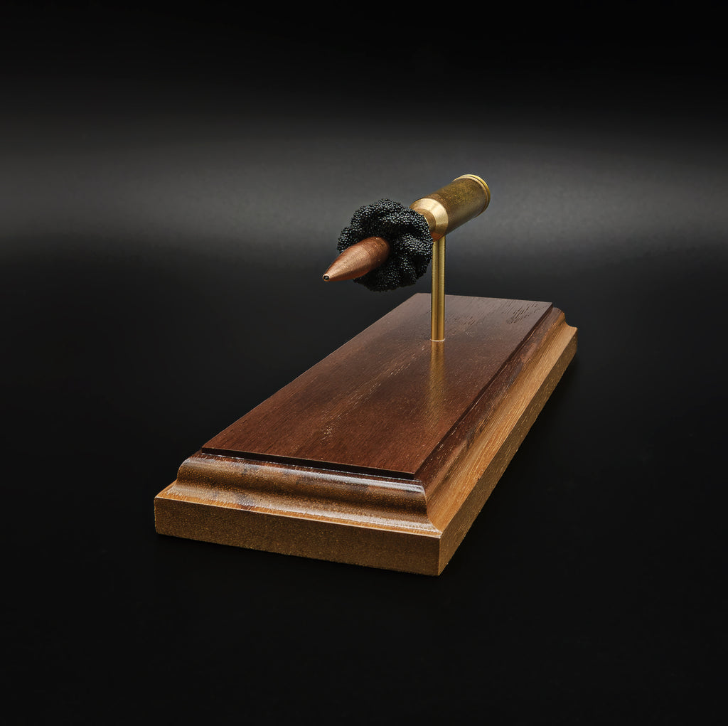Front-end perspective of an exploded 7mm Remington Magnum cartridge featuring the pointed 168gr Berger VLD bullet surrounded by simulated powder on an elegant walnut wood presentation base.