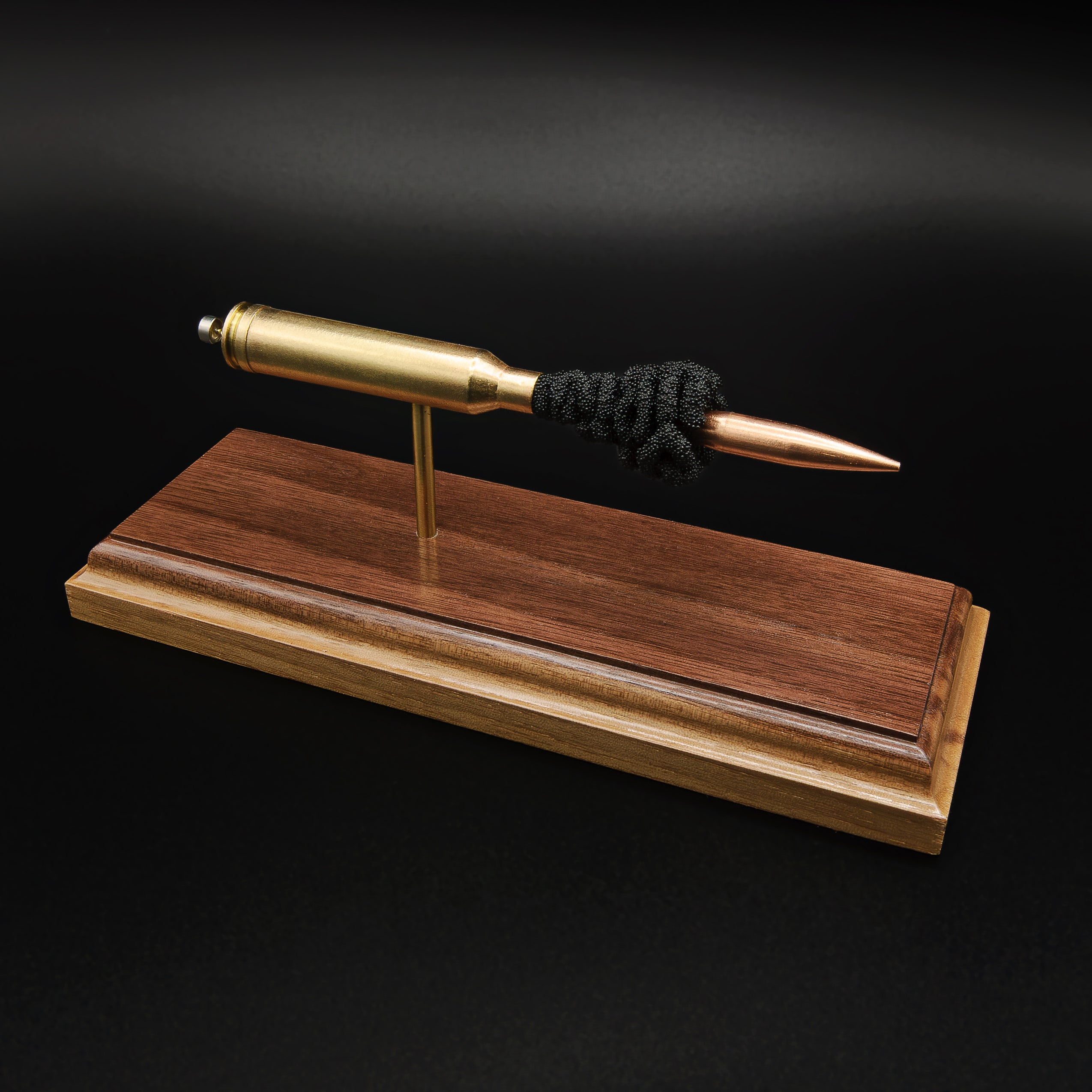 High front-left angle of a handcrafted 7mm Remington Magnum display showcasing the brass cartridge case, 168 grain Berger VLD bullet, exposed simulated powder, and walnut wood base against a black background.