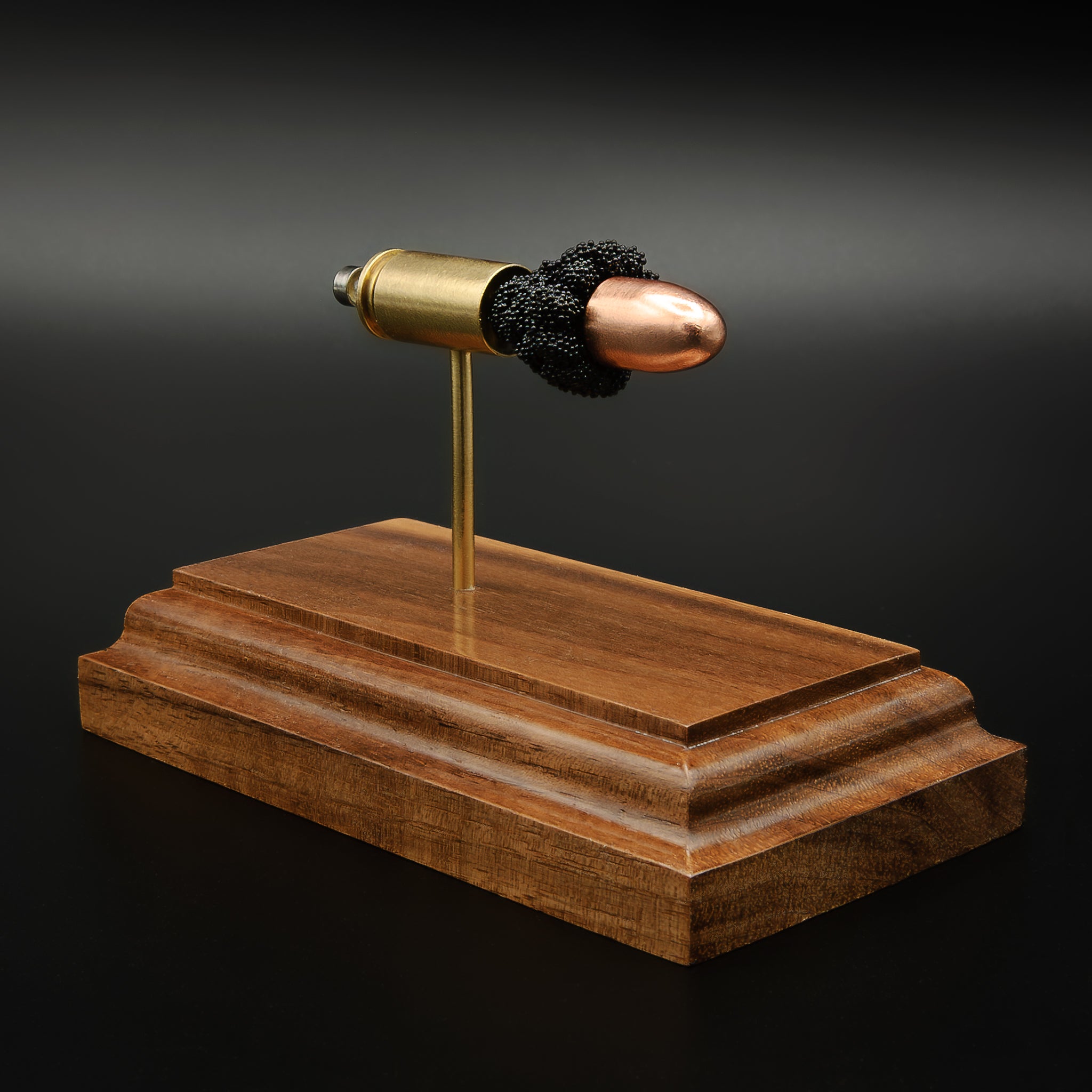 Angled view of 9mm FMJ cartridge display with separated components on walnut base