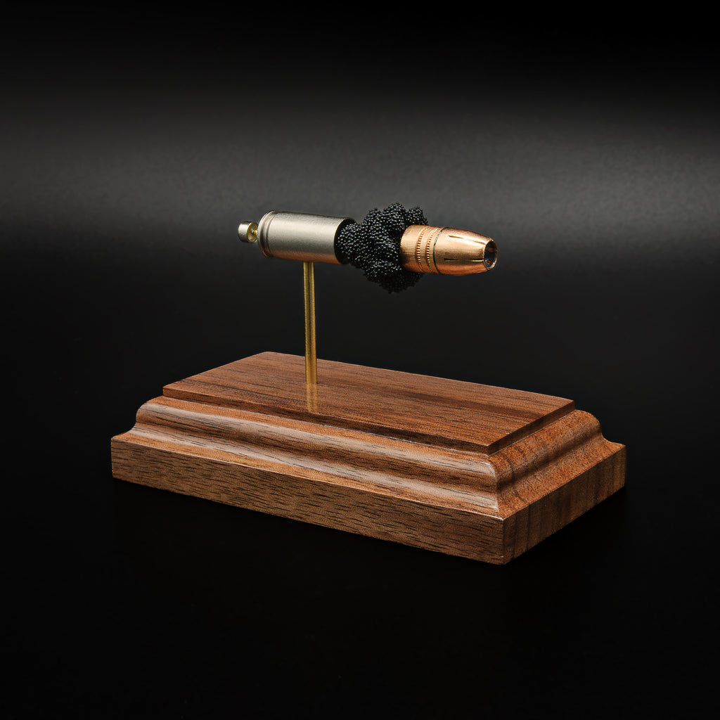 Right-front angle of an exploded 9mm Luger display showcasing the Federal 147gr HST hollow point bullet, exposed simulated powder, nickel-plated case, and handcrafted walnut wood base.