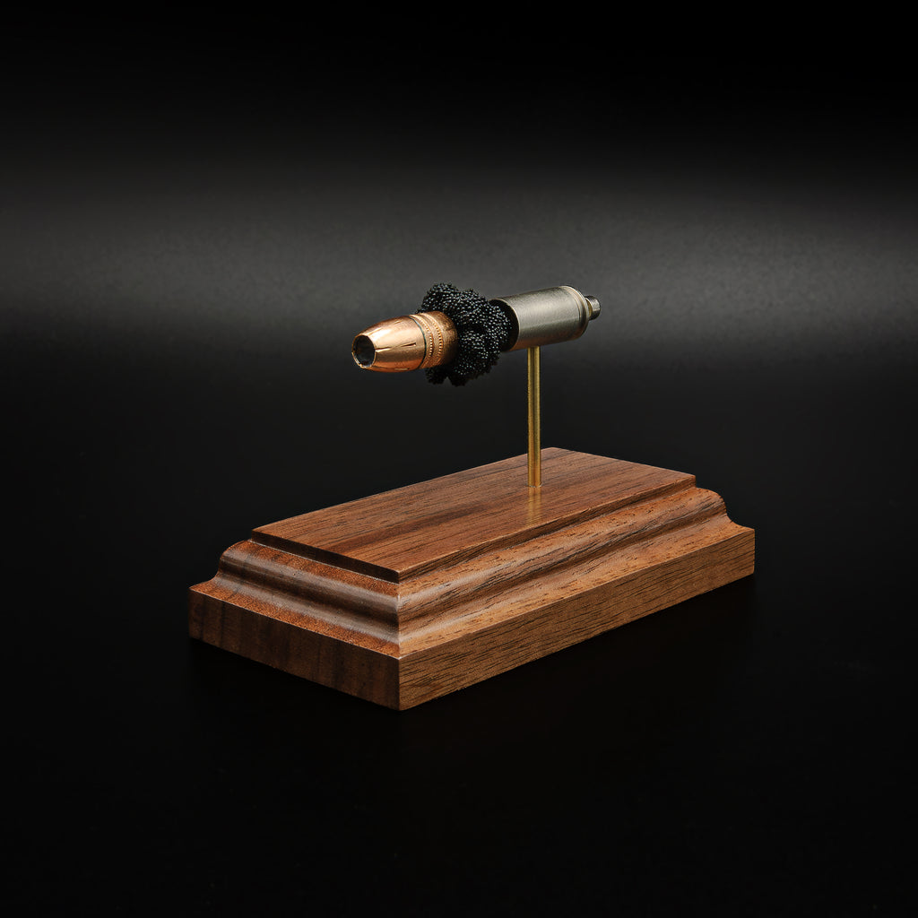 Rear-left three-quarter view of a 9mm Luger cartridge display highlighting the case head, primer assembly, Federal 147 grain HST hollow point bullet, and simulated powder on a walnut presentation base.