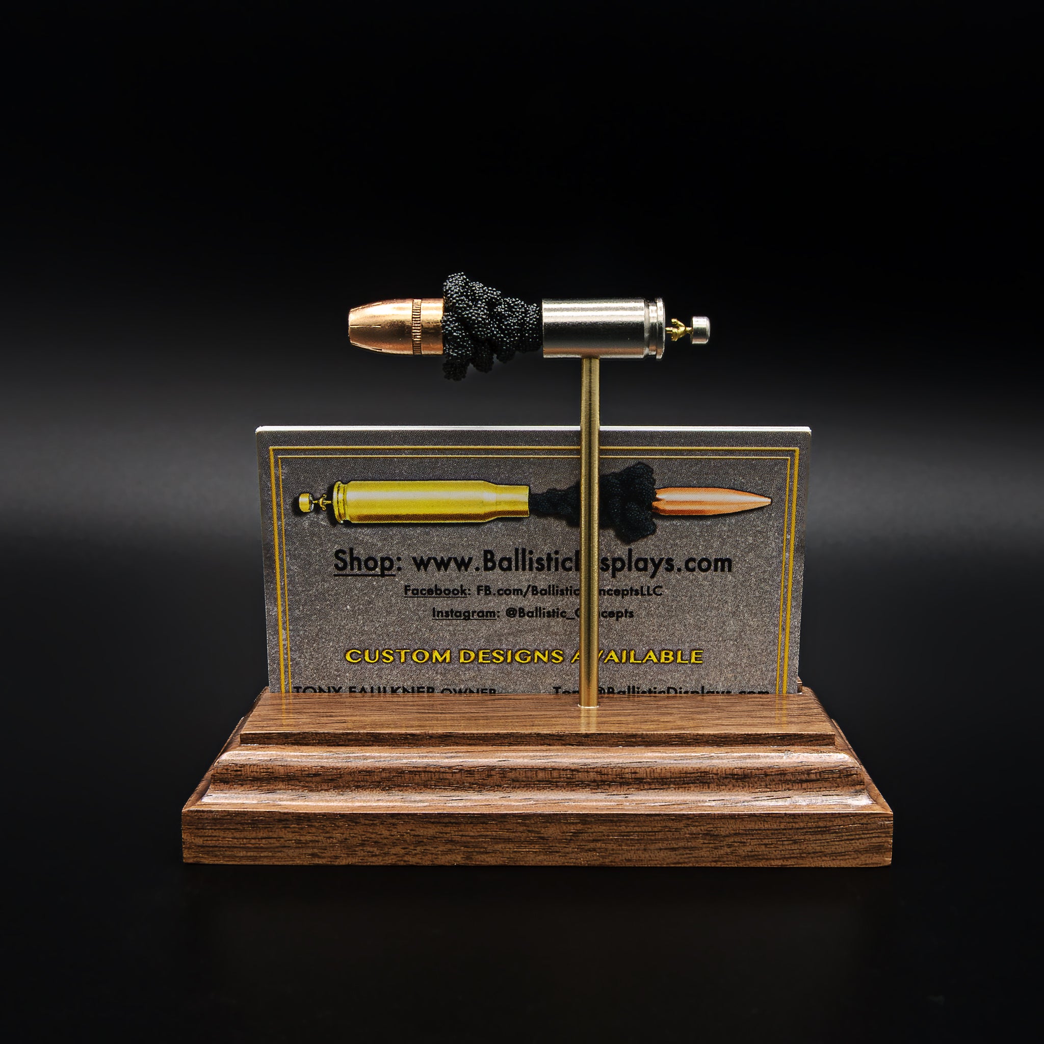 Rear view of a 9mm cartridge display with separated components mounted on rods, positioned above a business card holder cut into the base
