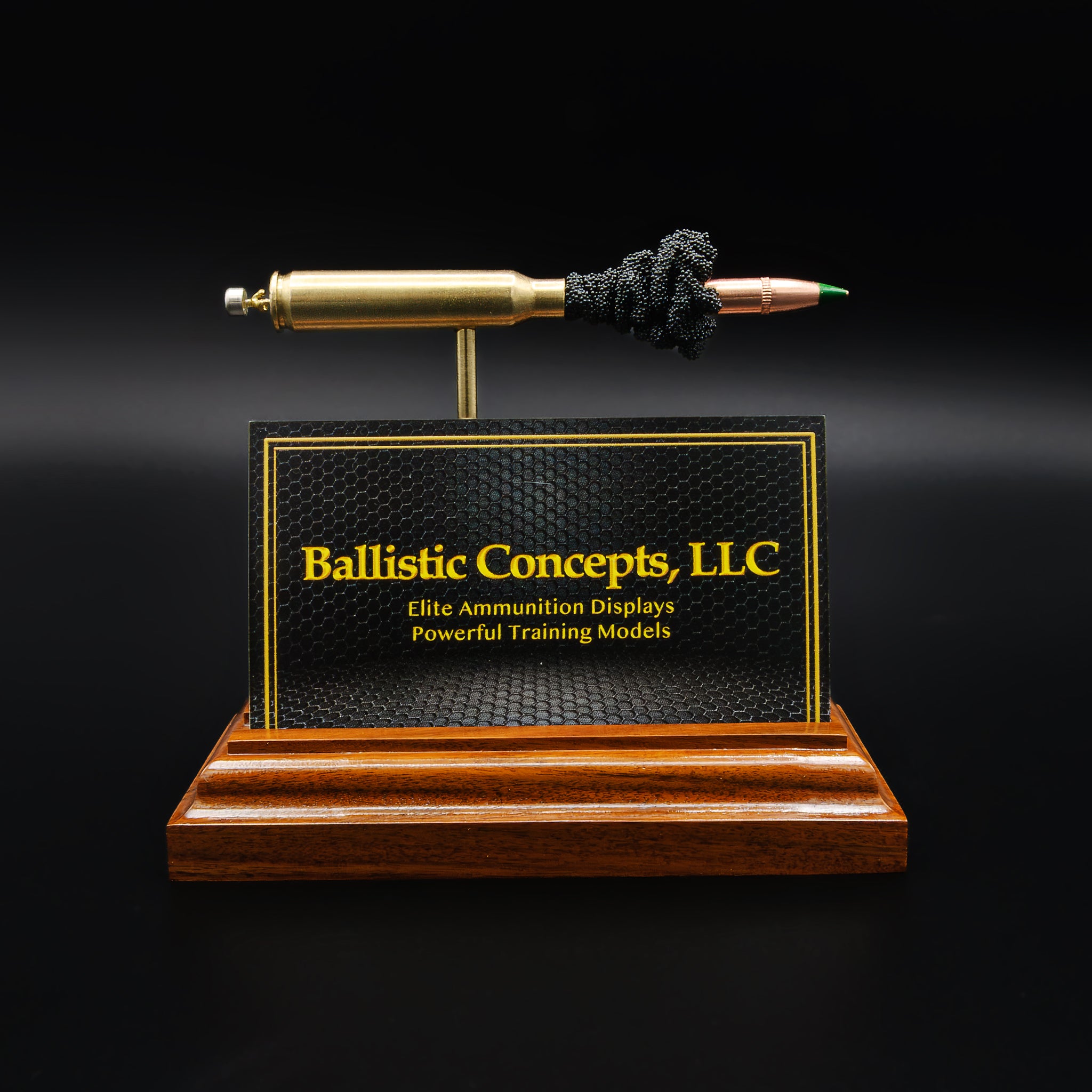 Desk display combining rifle cartridge anatomy model with business card holder slot on a rosewood base.