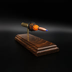 Top angled view of cartridge anatomy display showing spatial separation of case, powder cluster, and projectile on walnut base