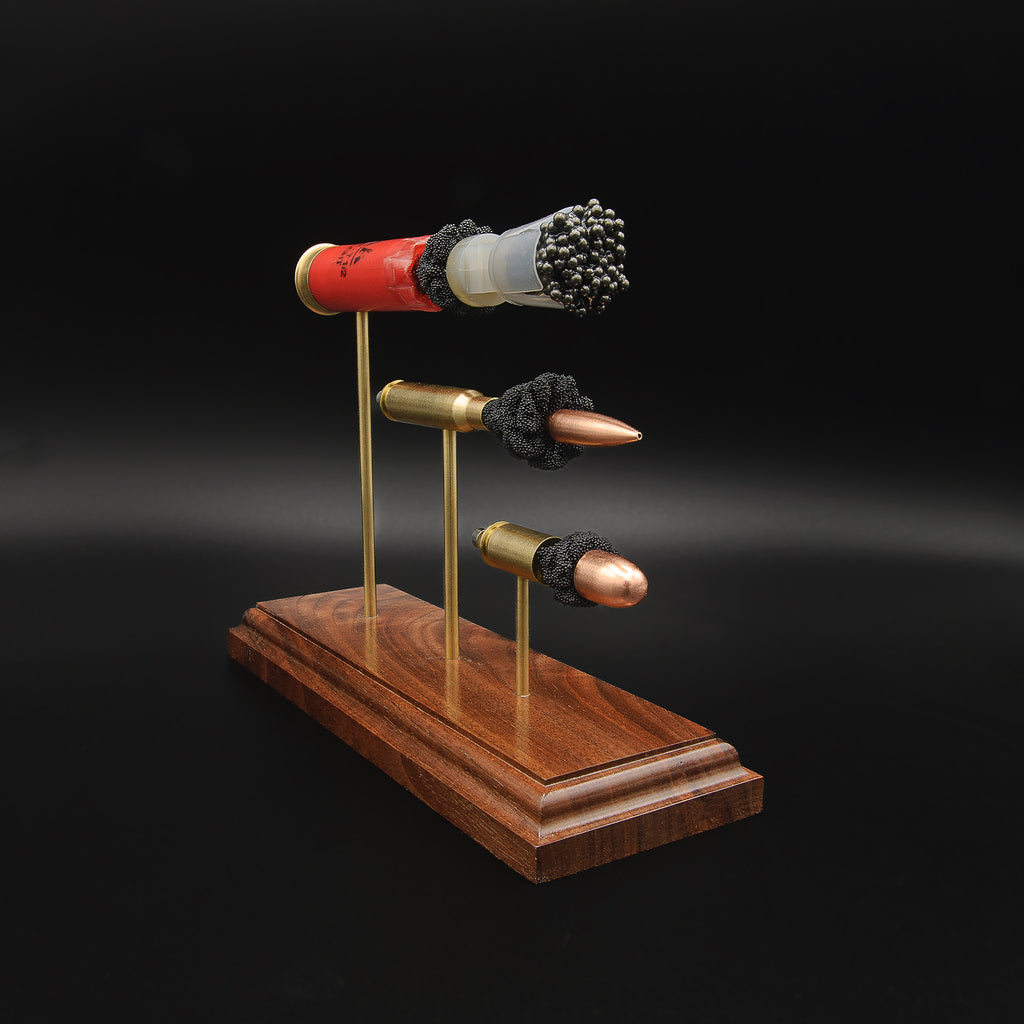 Three-quarter view of a 3-Gun Heavy Metal cartridge anatomy display featuring 12 gauge birdshot, 308 Winchester and 45 Auto on brass supports.
