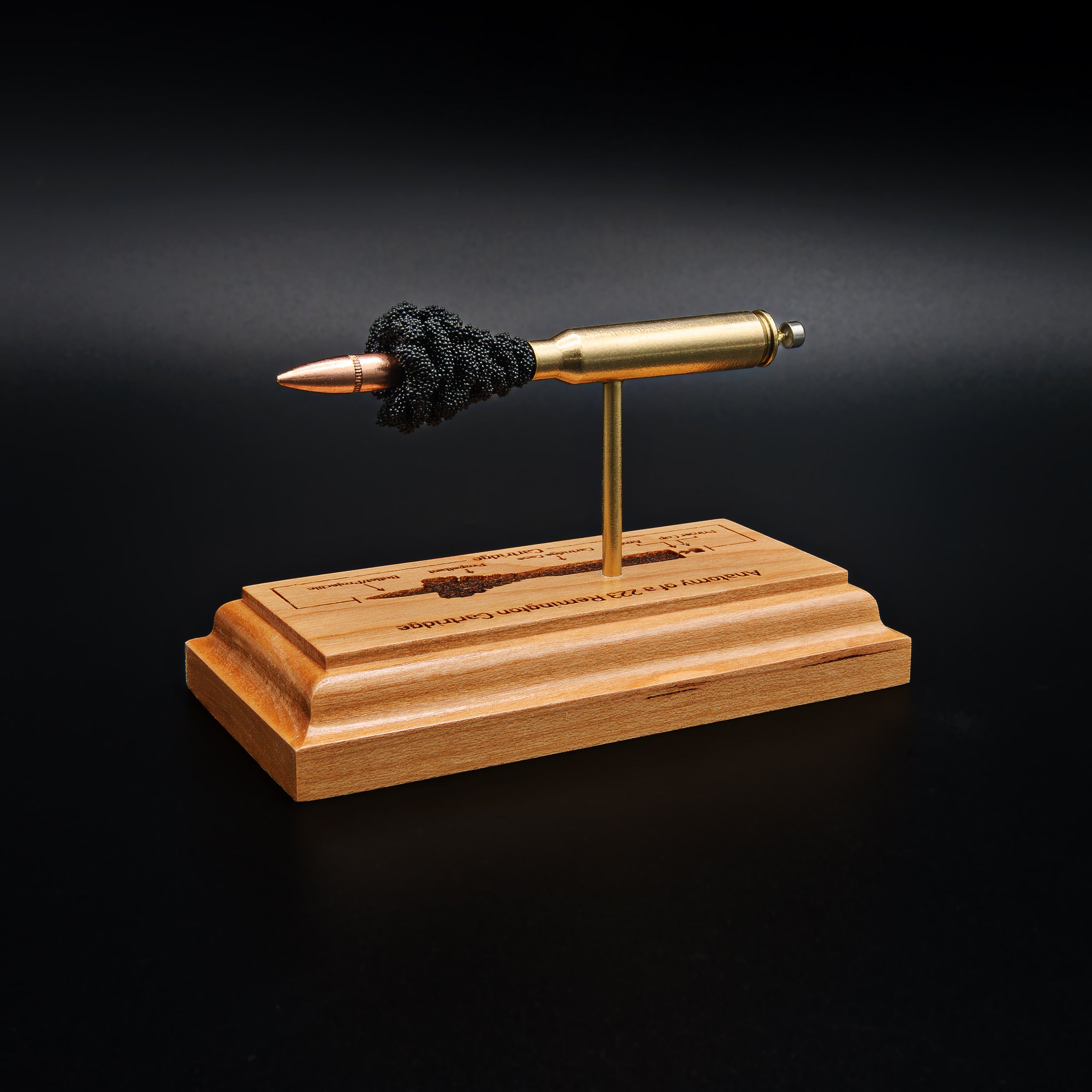 Opposite side view of a .223 Remington FMJ cartridge anatomy display showing the primer cup, anvil, cartridge case, simulated powder, and projectile on a cherry wood base with an engraved anatomy diagram.