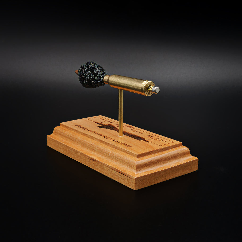 rear angled view of a .223 Remington FMJ cartridge anatomy display with the primer cup, anvil, cartridge case, simulated powder, and projectile mounted on a cherry wood base with an engraved anatomy diagram.