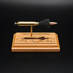 Front view of a .223 Remington FMJ cartridge anatomy display showing the primer cup, anvil, cartridge case, simulated powder, and projectile on a cherry wood base with an engraved anatomy diagram.