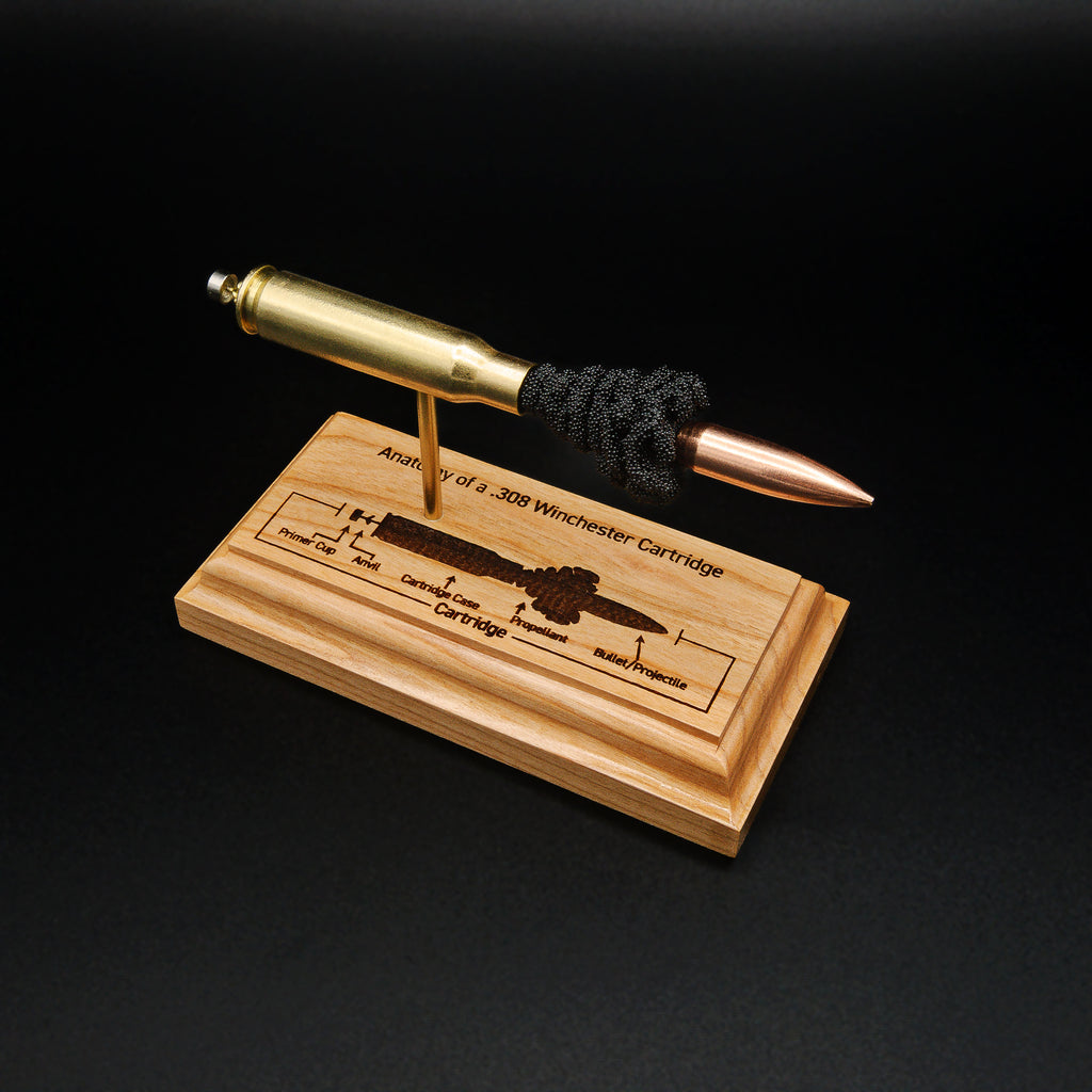 Angled front view of a .308 Winchester cartridge anatomy display featuring a 168gr Sierra MatchKing HPBT bullet, simulated powder, and a laser-engraved anatomy diagram on a handcrafted cherry wood base.