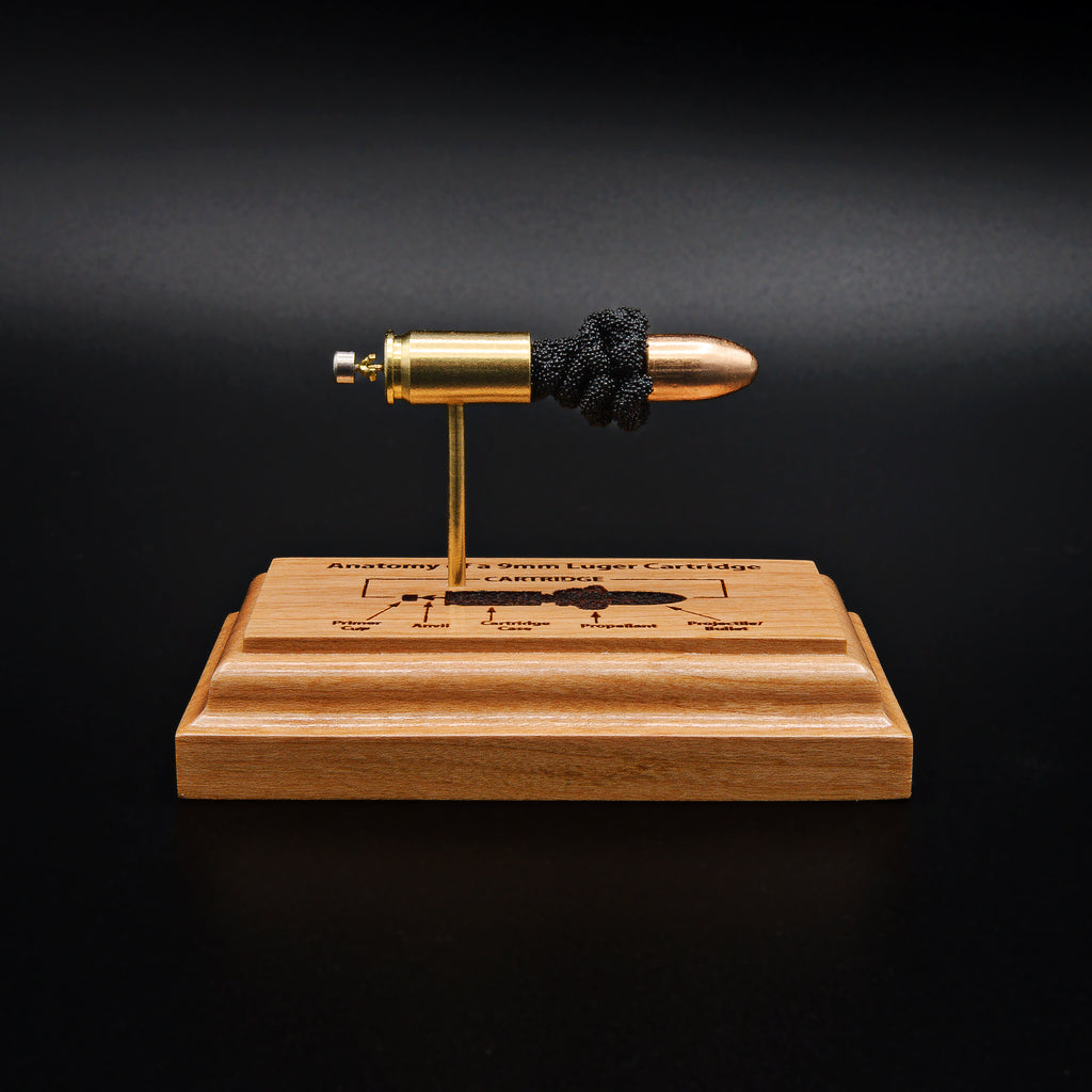 Front view of a handcrafted 9mm Luger cartridge anatomy display featuring a 115gr Sierra FMJ bullet with an engraved anatomy diagram showing the primer cup, anvil, cartridge case, powder, and projectile that is mounted on a solid cherry wood base.